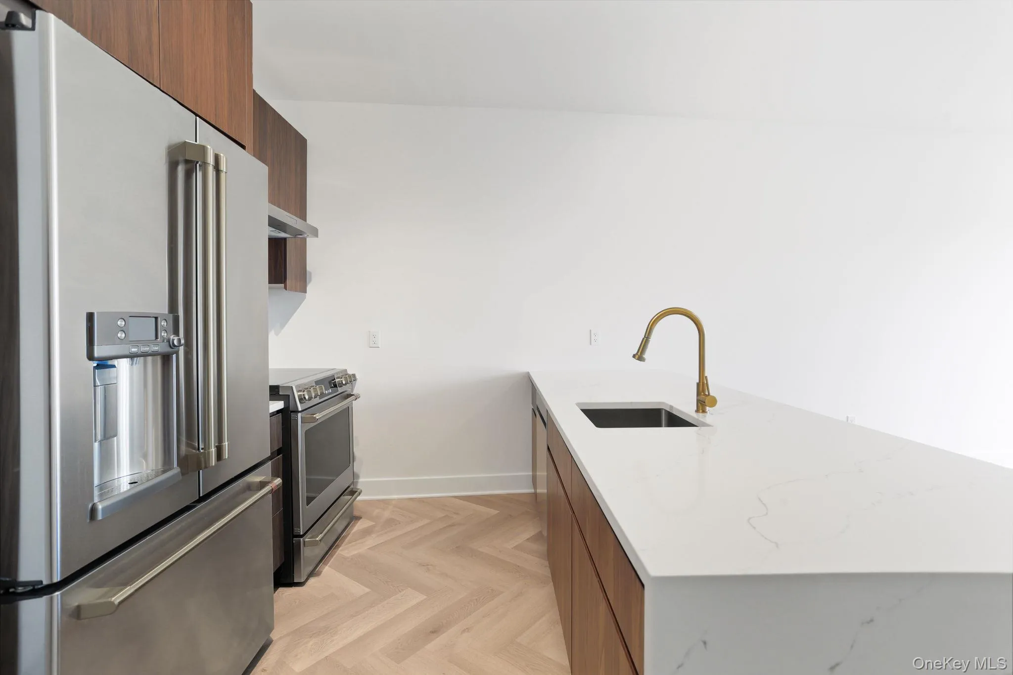 Kitchen with stainless steel appliances, a peninsula, brown cabinetry, light stone counters, and modern cabinets Kitchen with stainless steel appliances, a peninsula, brown cabinetry, light stone counters, and modern cabinets