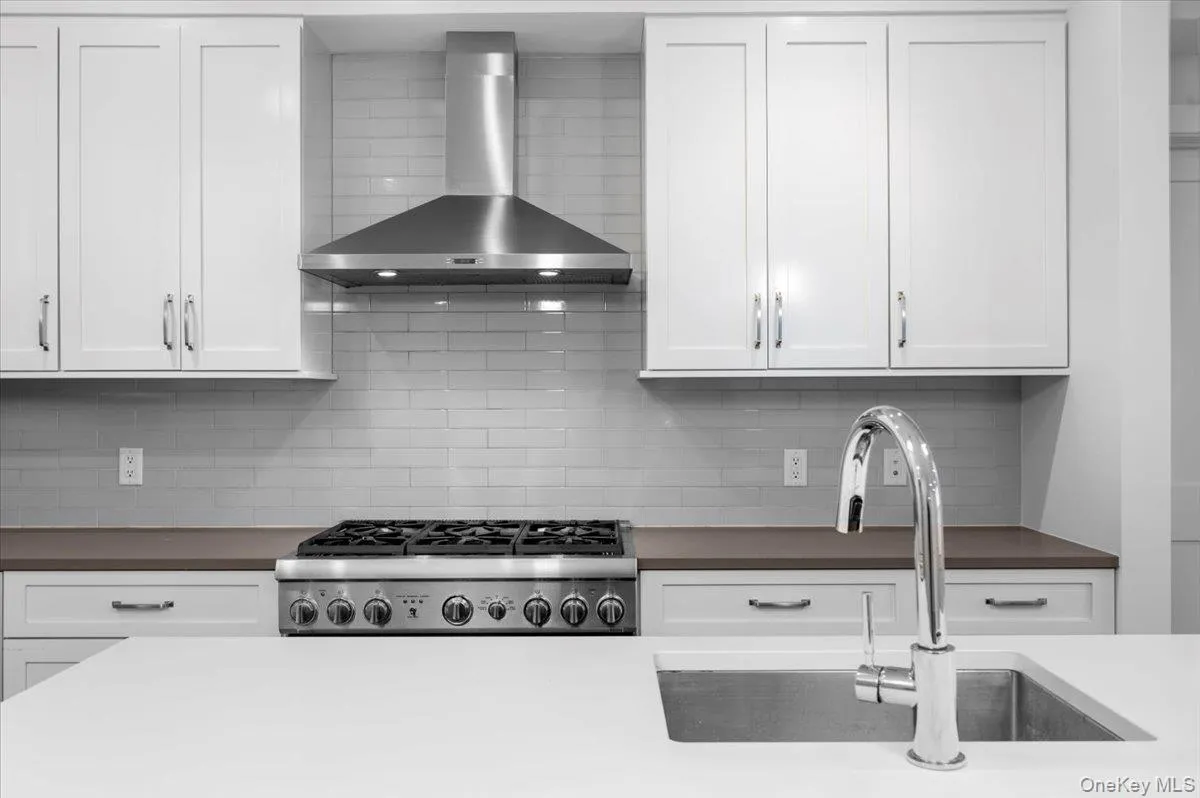 Kitchen with wall chimney range hood, white cabinetry, and decorative backsplash Kitchen with wall chimney range hood, white cabinetry, and decorative backsplash