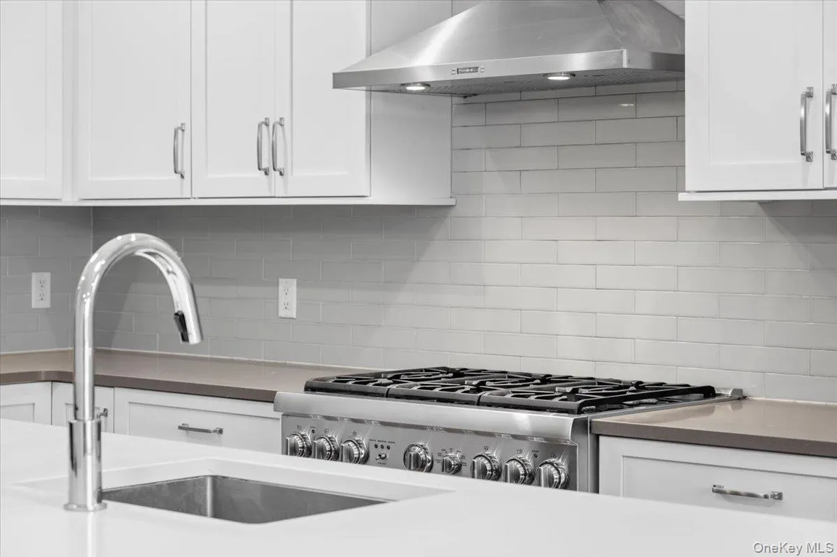 Kitchen with wall chimney exhaust hood, white cabinets, gas stove, and backsplash Kitchen with wall chimney exhaust hood, white cabinets, gas stove, and backsplash