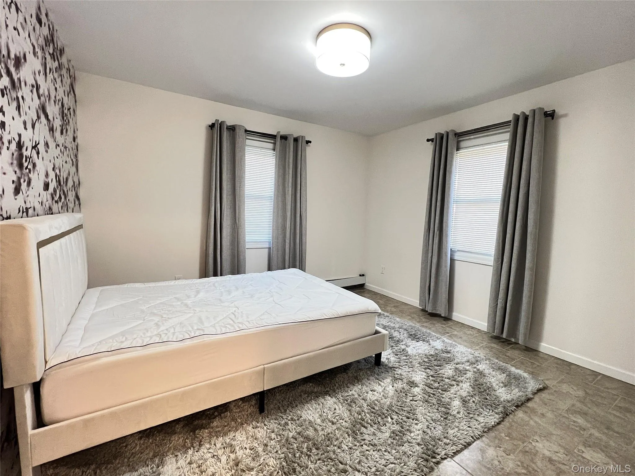 Bedroom featuring multiple windows and a baseboard heating unit Bedroom featuring multiple windows and a baseboard heating unit