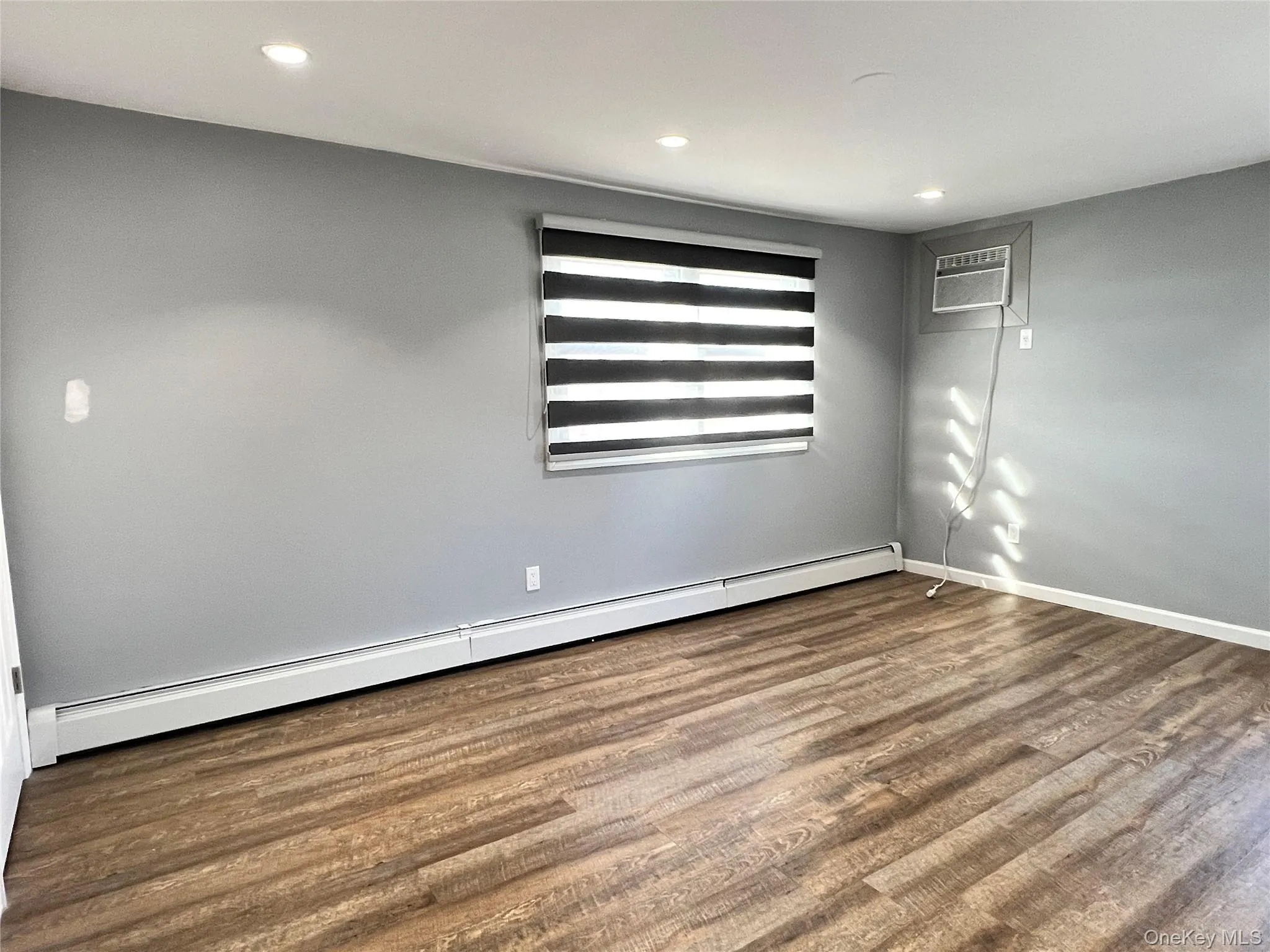 Unfurnished room featuring a baseboard heating unit, wood finished floors, recessed lighting, and a wall mounted air conditioner Unfurnished room featuring a baseboard heating unit, wood finished floors, recessed lighting, and a wall mounted air conditioner