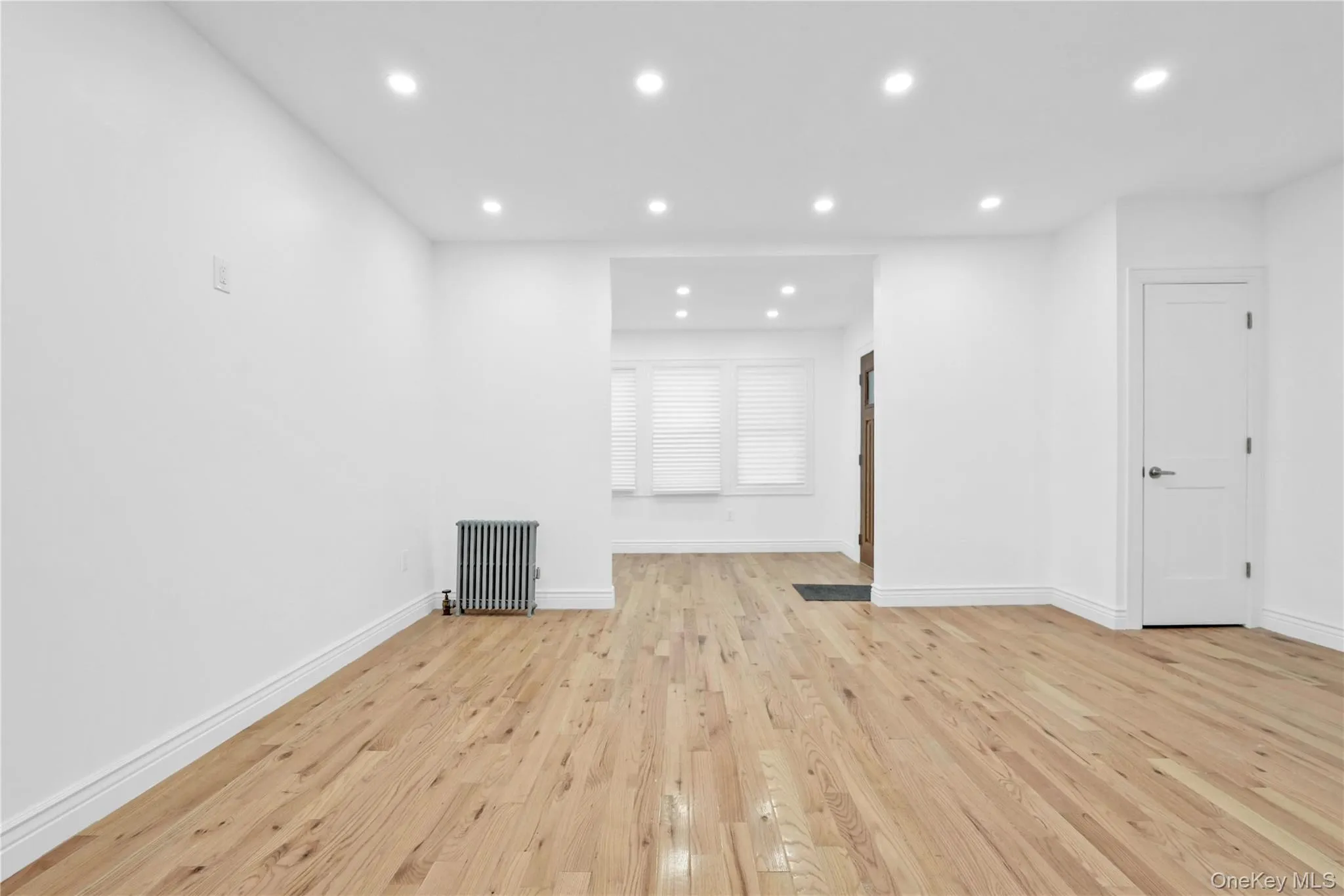 Unfurnished living room featuring recessed lighting, light wood-style flooring, and radiator Unfurnished living room featuring recessed lighting, light wood-style flooring, and radiator