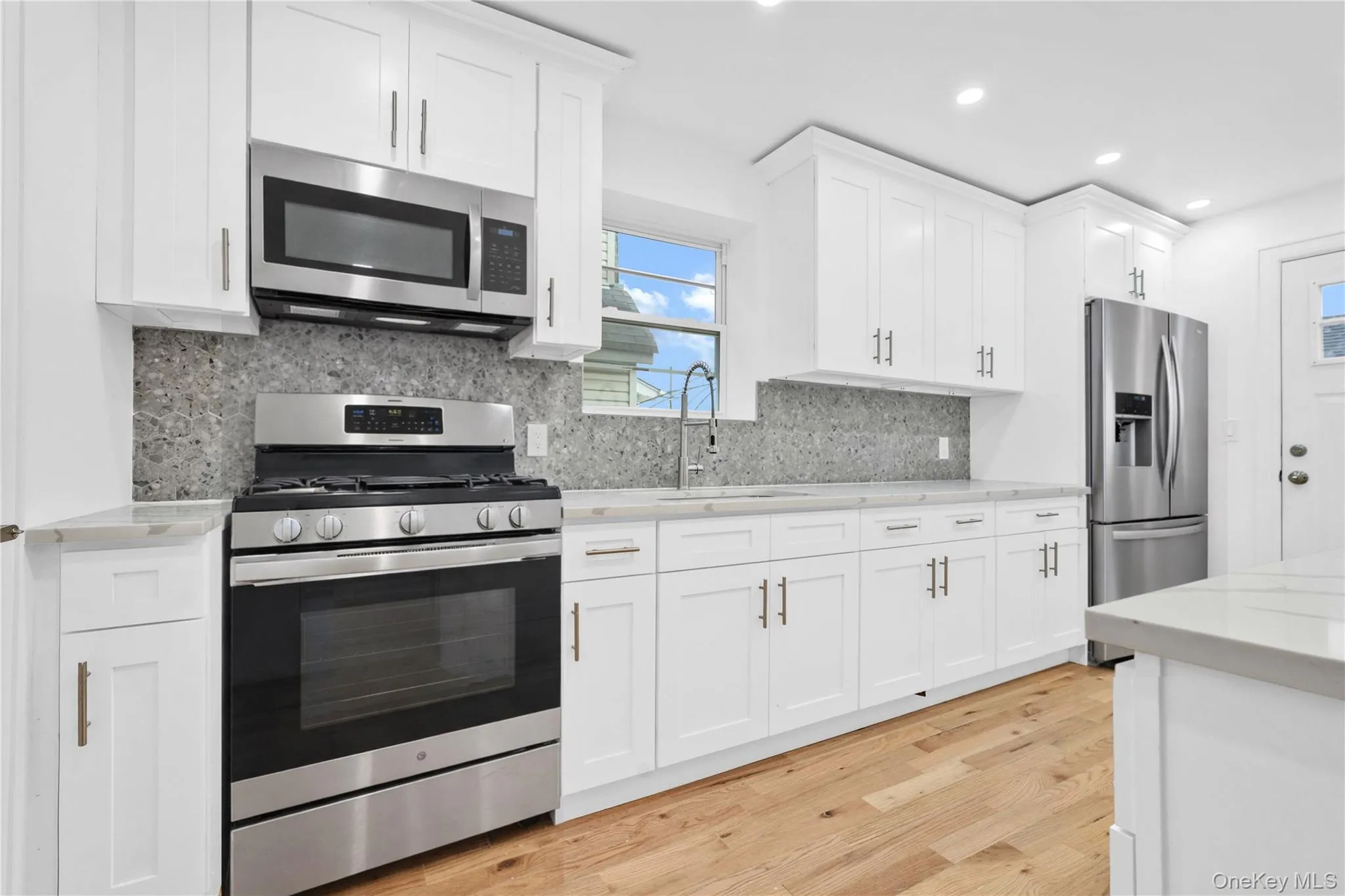 Kitchen featuring stainless steel appliances, white cabinetry, light wood finished floors, light stone counters, and recessed lighting Kitchen featuring stainless steel appliances, white cabinetry, light wood finished floors, light stone counters, and recessed lighting