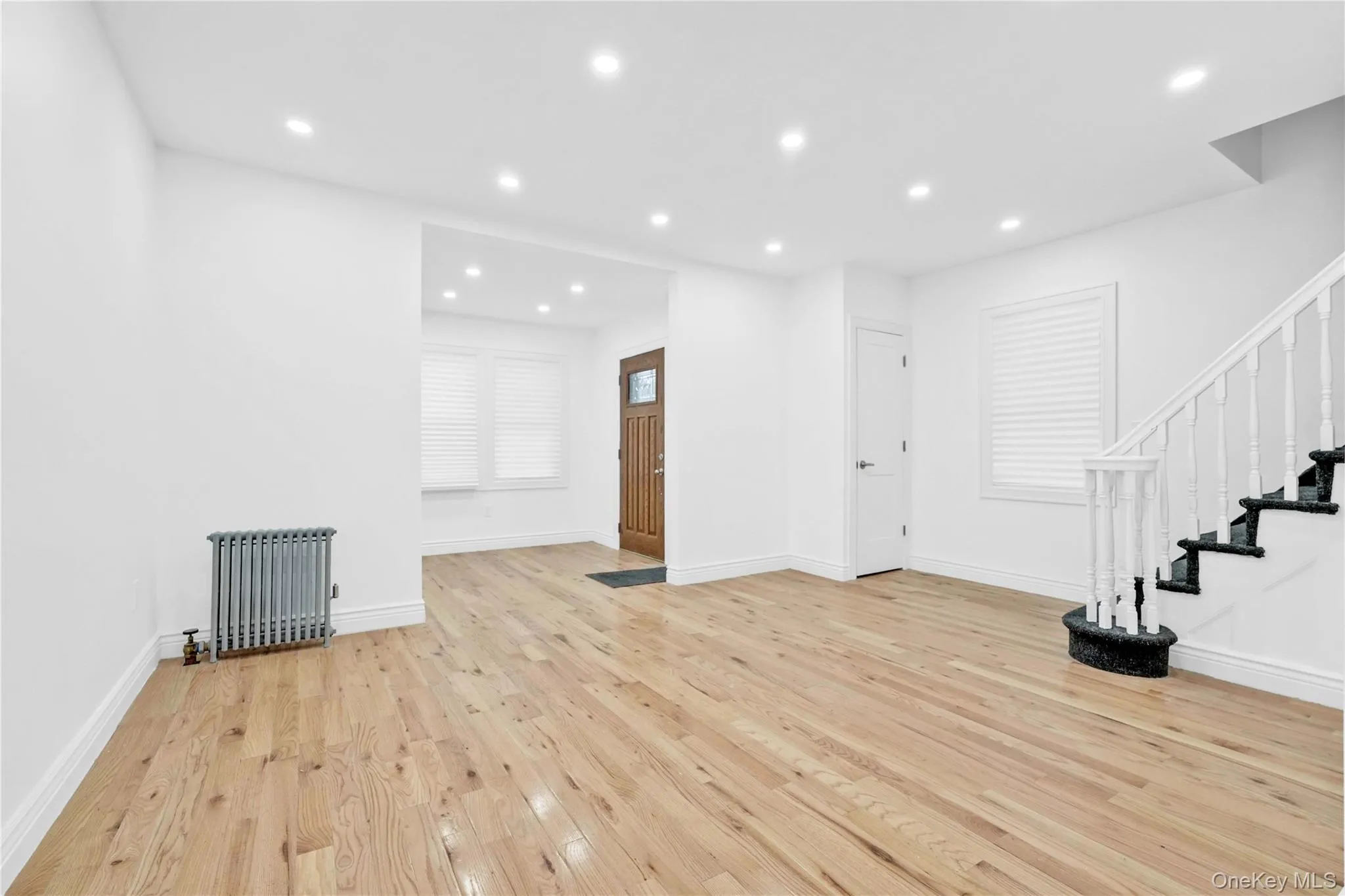 Unfurnished living room featuring stairs, radiator, light wood-type flooring, and recessed lighting Unfurnished living room featuring stairs, radiator, light wood-type flooring, and recessed lighting
