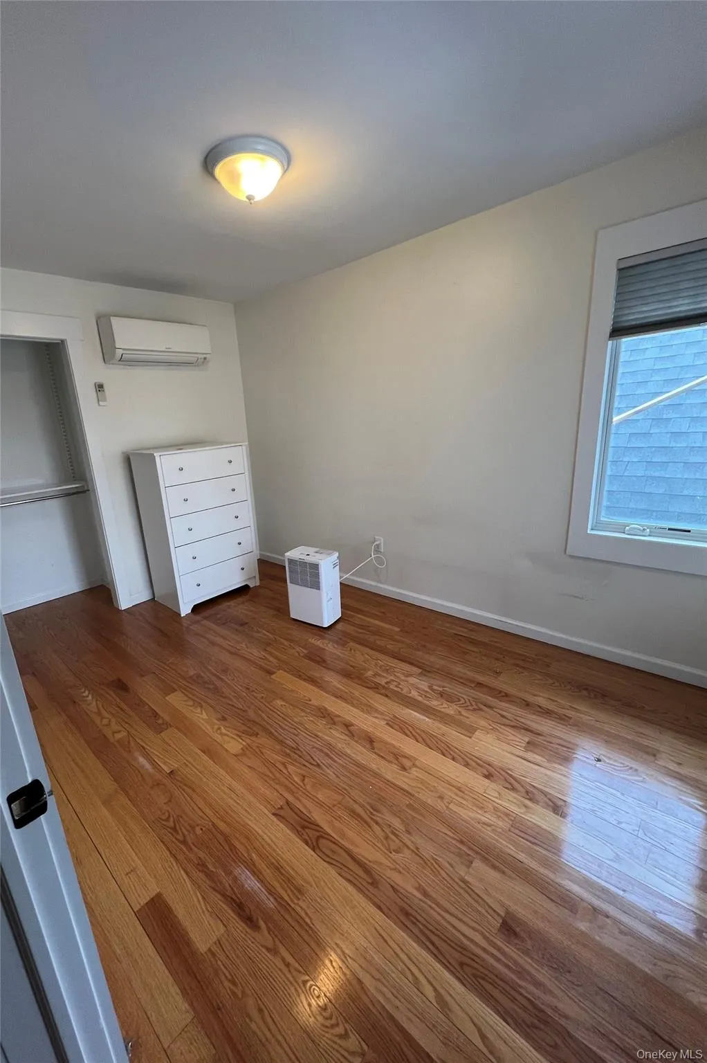 Unfurnished bedroom with an AC wall unit, baseboards, and wood finished floors Unfurnished bedroom with an AC wall unit, baseboards, and wood finished floors