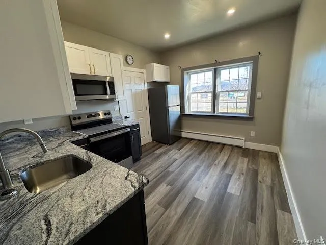 Kitchen with white cabinets, appliances with stainless steel finishes, light stone countertops, dark wood-style flooring, and electric baseboard heating units. Kitchen with white cabinets, appliances with stainless steel finishes, light stone countertops, dark wood-style flooring, and electric baseboard heating units.