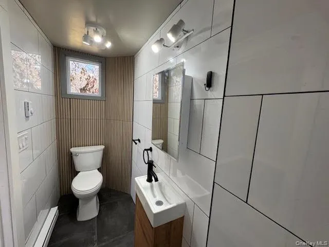 Half bathroom with vanity, dark tile patterned flooring, baseboard heating, and tile walls Half bathroom with vanity, dark tile patterned flooring, baseboard heating, and tile walls