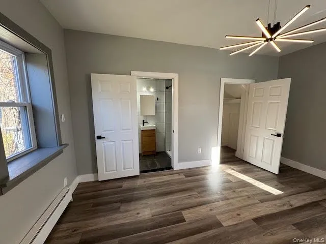 Unfurnished bedroom featuring a baseboard heating unit, a walk in closet, dark wood-type flooring, ceiling fan, and ensuite bathroom Unfurnished bedroom featuring a baseboard heating unit, a walk in closet, dark wood-type flooring, ceiling fan, and ensuite bathroom
