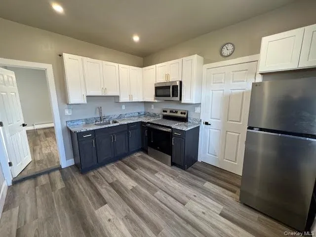 Kitchen featuring white cabinetry, appliances with stainless steel finishes, ceramic tile floors, a baseboard heating unit, and granite countertops Kitchen featuring white cabinetry, appliances with stainless steel finishes, ceramic tile floors, a baseboard heating unit, and granite countertops