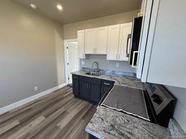 Kitchen with white cabinets, light stone countertops, dark wood-style flooring, and electric range Kitchen with white cabinets, light stone countertops, dark wood-style flooring, and electric range