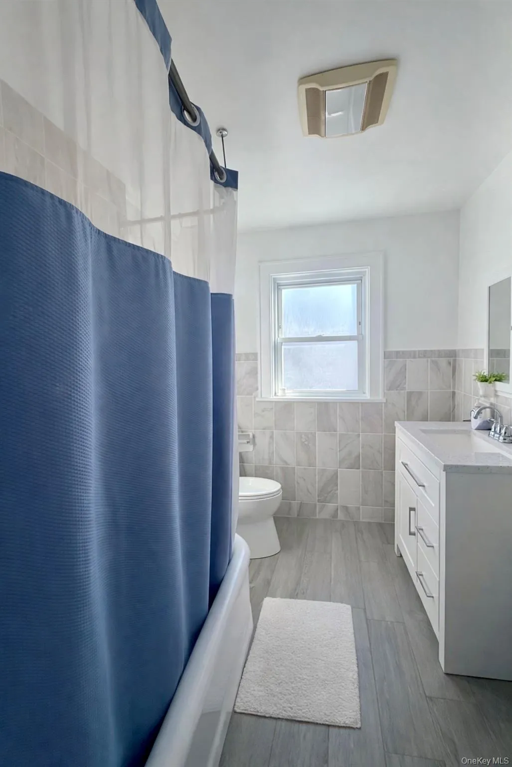 Full bathroom with tile walls, wainscoting, shower / bath combo with shower curtain, vanity, and light wood-type flooring Full bathroom with tile walls, wainscoting, shower / bath combo with shower curtain, vanity, and light wood-type flooring
