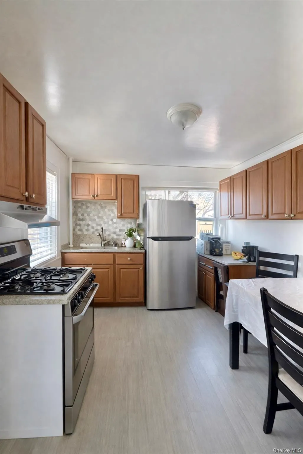 Kitchen with stainless steel appliances, light countertops, under cabinet range hood, brown cabinetry, and healthy amount of natural light Kitchen with stainless steel appliances, light countertops, under cabinet range hood, brown cabinetry, and healthy amount of natural light