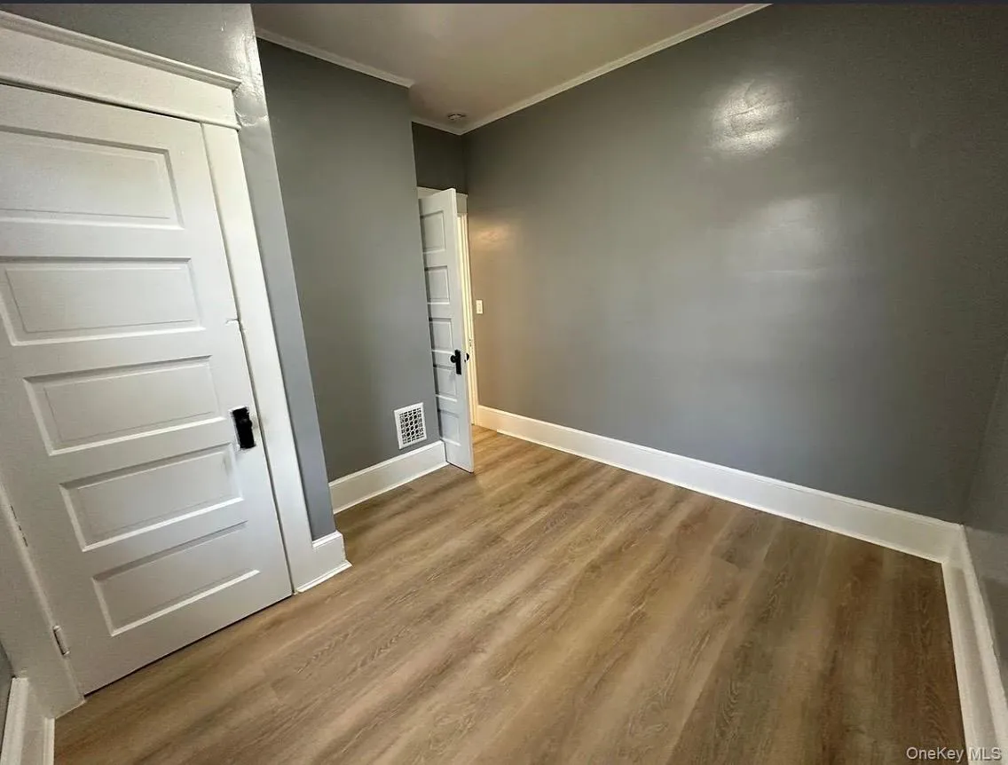 Unfurnished bedroom with ornamental molding, wood finished floors, and a closet Unfurnished bedroom with ornamental molding, wood finished floors, and a closet