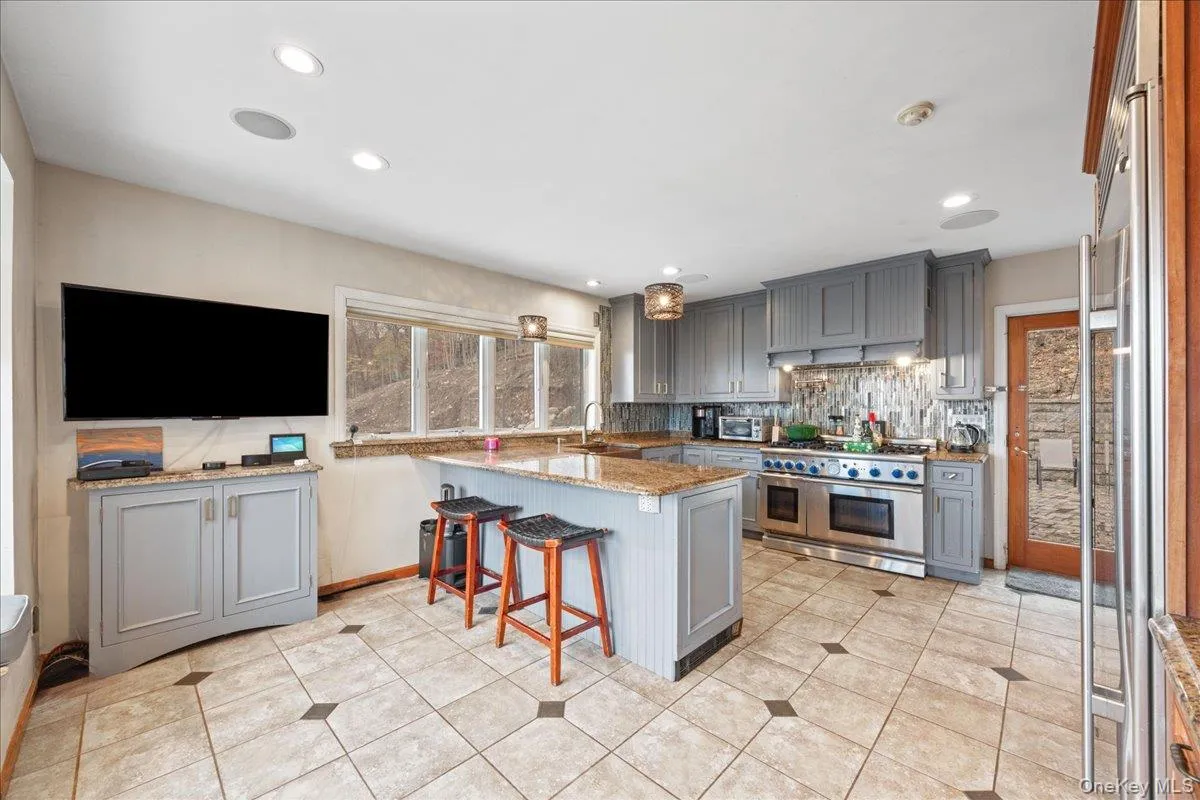 Kitchen with gray cabinets, a kitchen bar, high end appliances, recessed lighting, and light stone counters Kitchen with gray cabinets, a kitchen bar, high end appliances, recessed lighting, and light stone counters