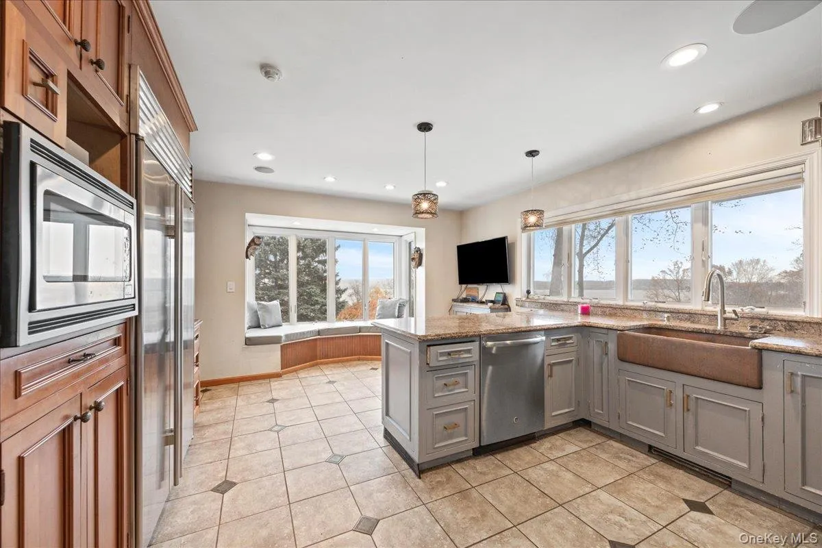 Kitchen featuring a peninsula, gray cabinetry, light stone countertops, built in appliances, and hanging light fixtures Kitchen featuring a peninsula, gray cabinetry, light stone countertops, built in appliances, and hanging light fixtures