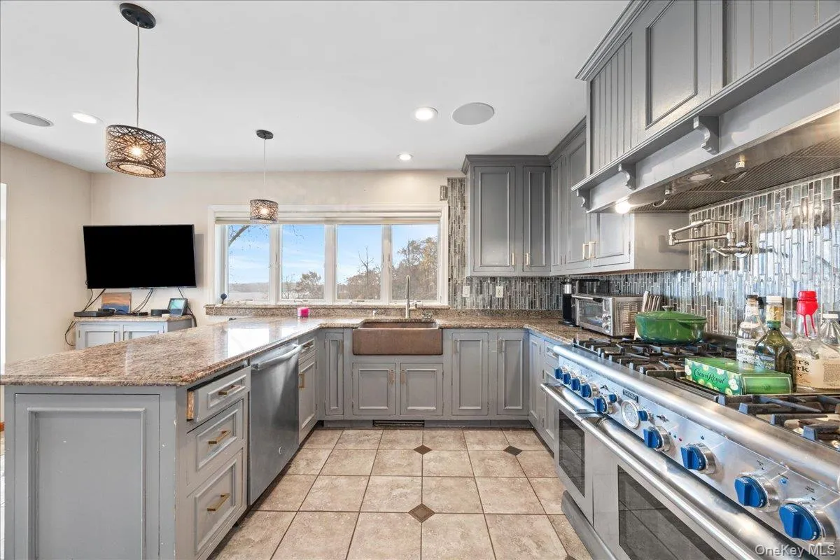 Kitchen featuring gray cabinets, appliances with stainless steel finishes, light stone countertops, ventilation hood, and decorative light fixtures Kitchen featuring gray cabinets, appliances with stainless steel finishes, light stone countertops, ventilation hood, and decorative light fixtures