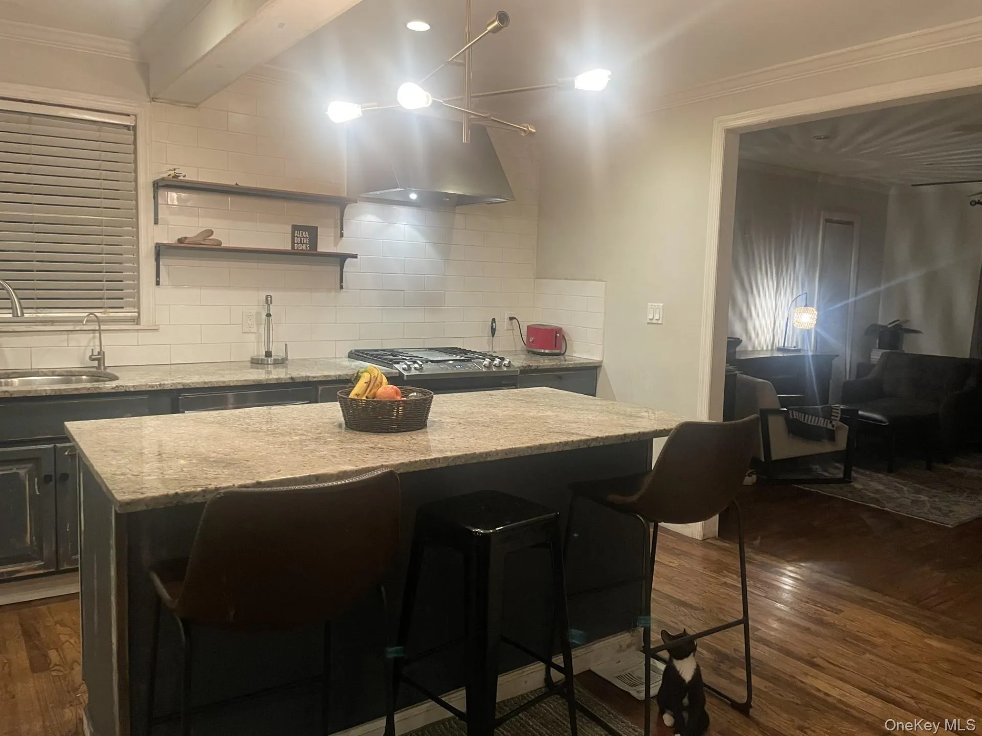 Kitchen featuring a kitchen bar, light stone countertops, dark wood-style floors, ornamental molding, and decorative backsplash Kitchen featuring a kitchen bar, light stone countertops, dark wood-style floors, ornamental molding, and decorative backsplash