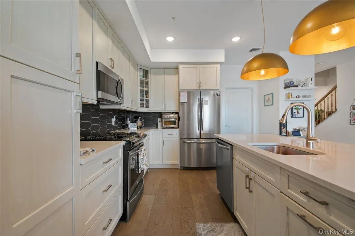 Kitchen with appliances with stainless steel finishes, hanging light fixtures, decorative backsplash, glass insert cabinets, and light stone countertops Kitchen with appliances with stainless steel finishes, hanging light fixtures, decorative backsplash, glass insert cabinets, and light stone countertops