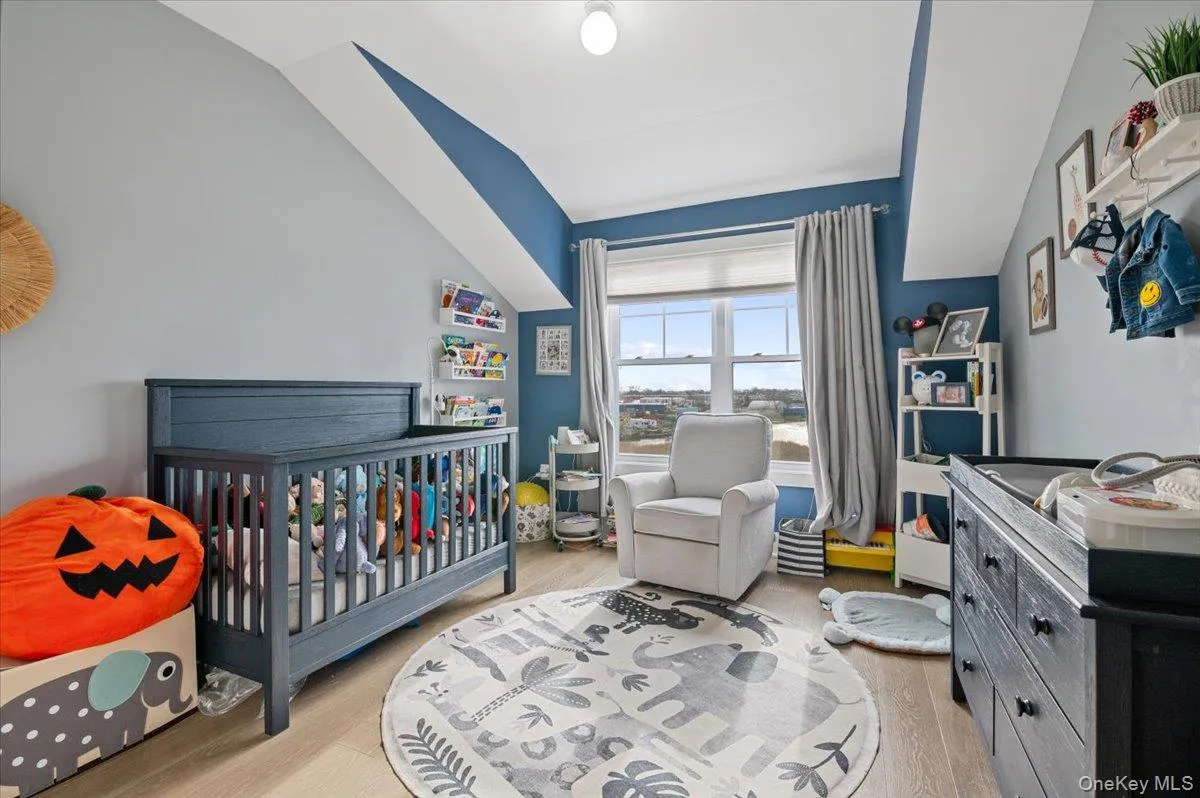 Bedroom featuring a nursery area, light wood-type flooring, and lofted ceiling Bedroom featuring a nursery area, light wood-type flooring, and lofted ceiling