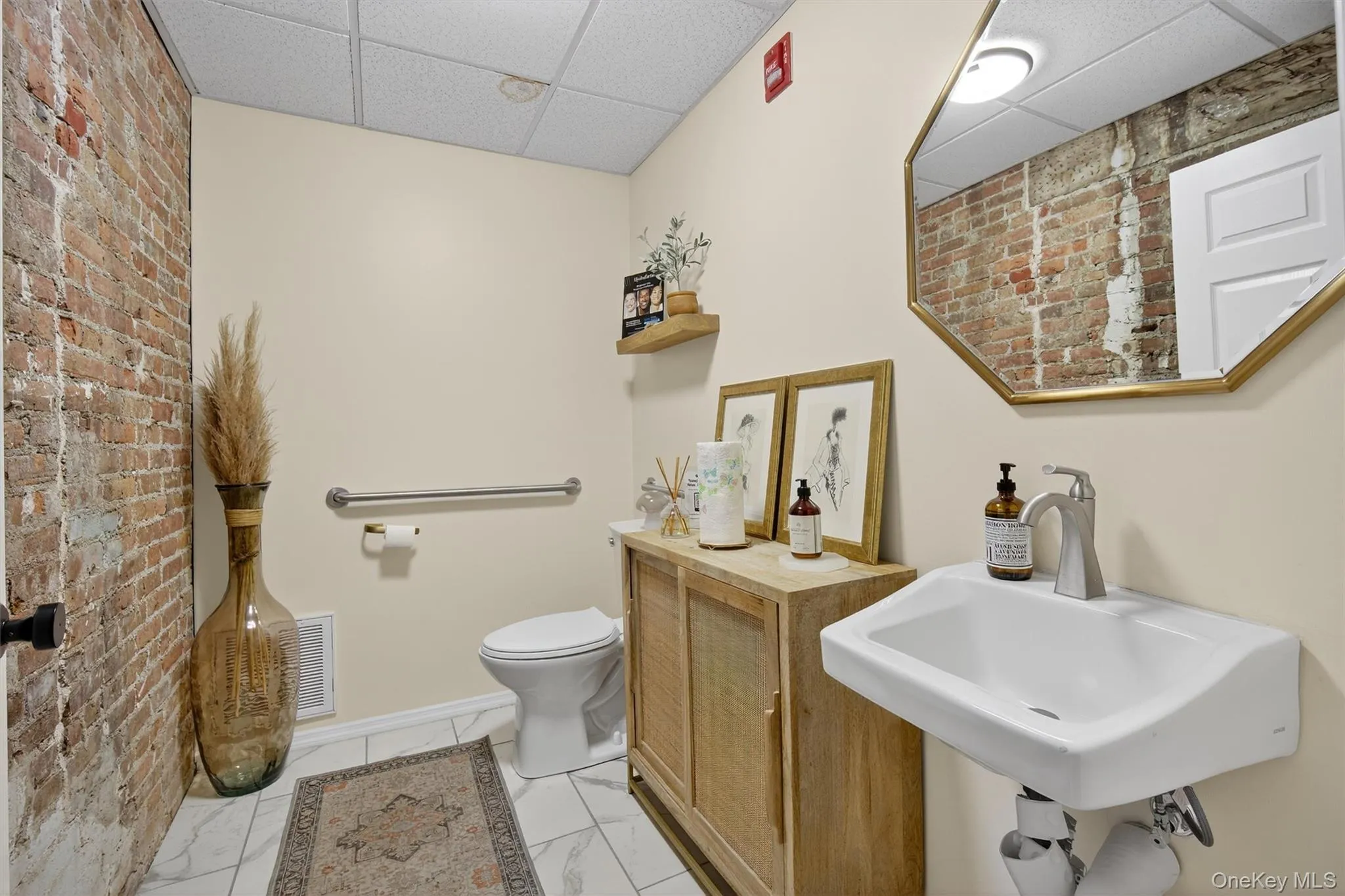 Half bathroom with brick wall, a drop ceiling, and light marble finish floors Half bathroom with brick wall, a drop ceiling, and light marble finish floors