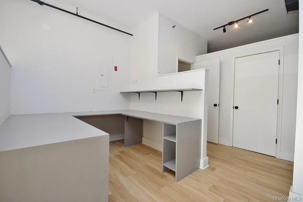 Unfurnished office with light wood-style flooring, rail lighting, and electric panel Unfurnished office with light wood-style flooring, rail lighting, and electric panel