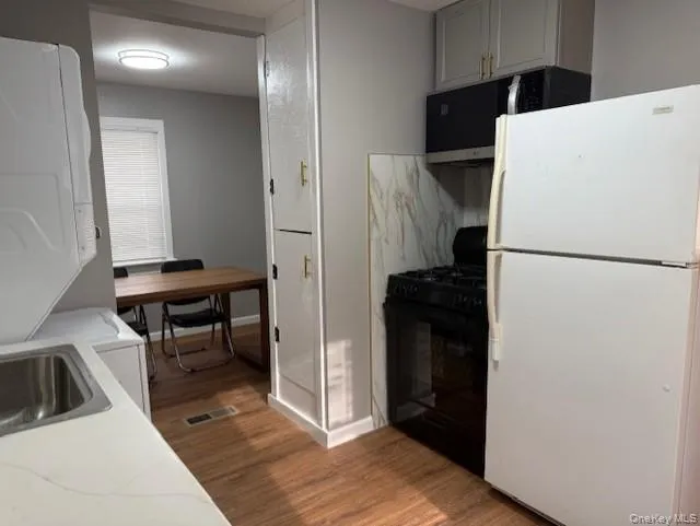 Kitchen featuring freestanding refrigerator, black range with gas stovetop, light countertops, dark wood finished floors, and stacked washing machine and dryer Kitchen featuring freestanding refrigerator, black range with gas stovetop, light countertops, dark wood finished floors, and stacked washing machine and dryer
