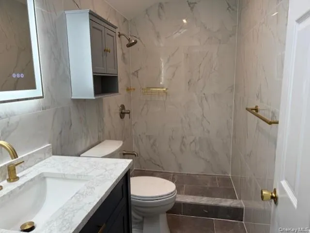 Full bathroom featuring tile walls, vanity, and a marble finish shower Full bathroom featuring tile walls, vanity, and a marble finish shower
