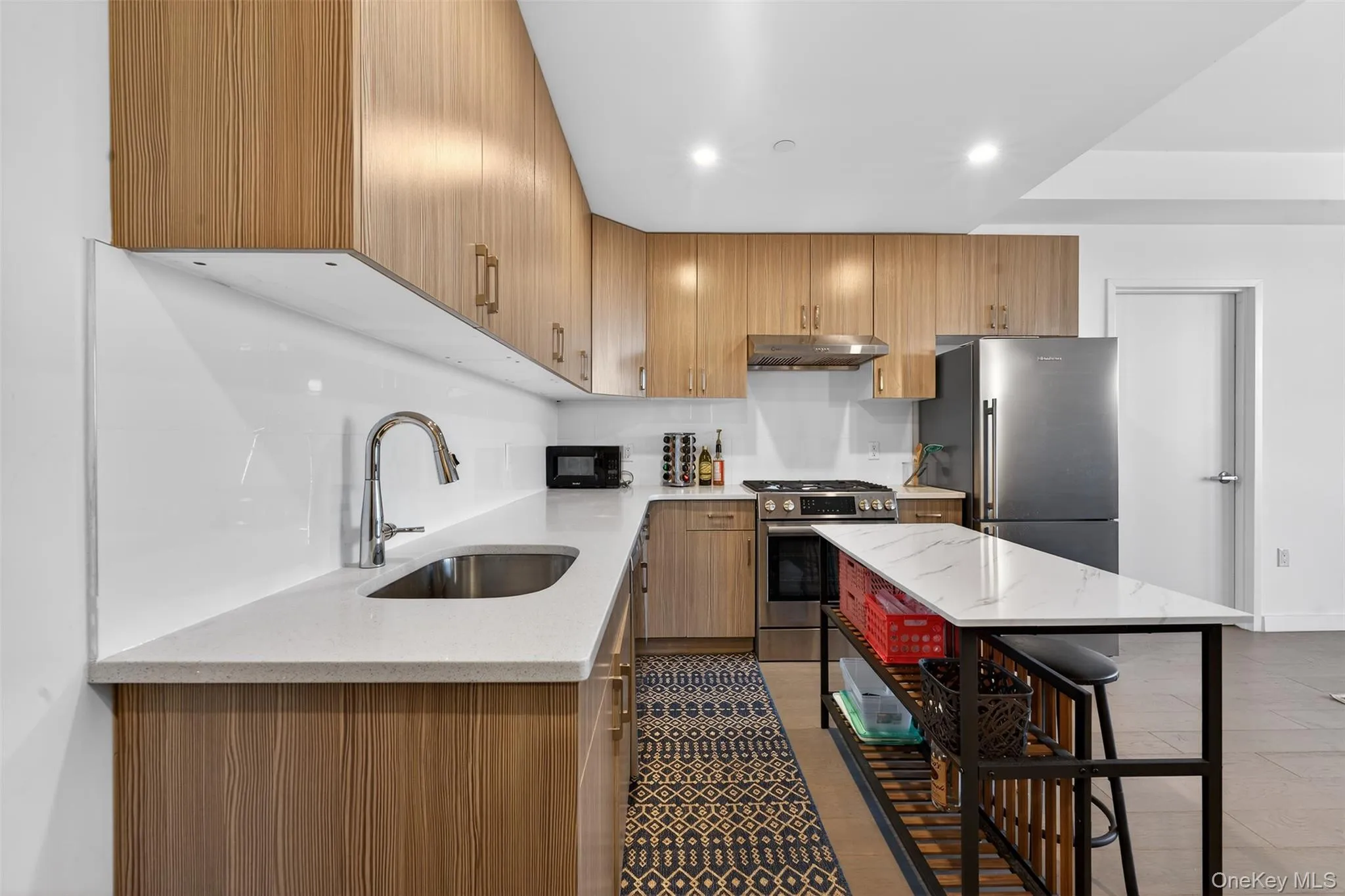 Kitchen with light stone countertops, appliances with stainless steel finishes, brown cabinetry, under cabinet range hood, and recessed lighting Kitchen with light stone countertops, appliances with stainless steel finishes, brown cabinetry, under cabinet range hood, and recessed lighting