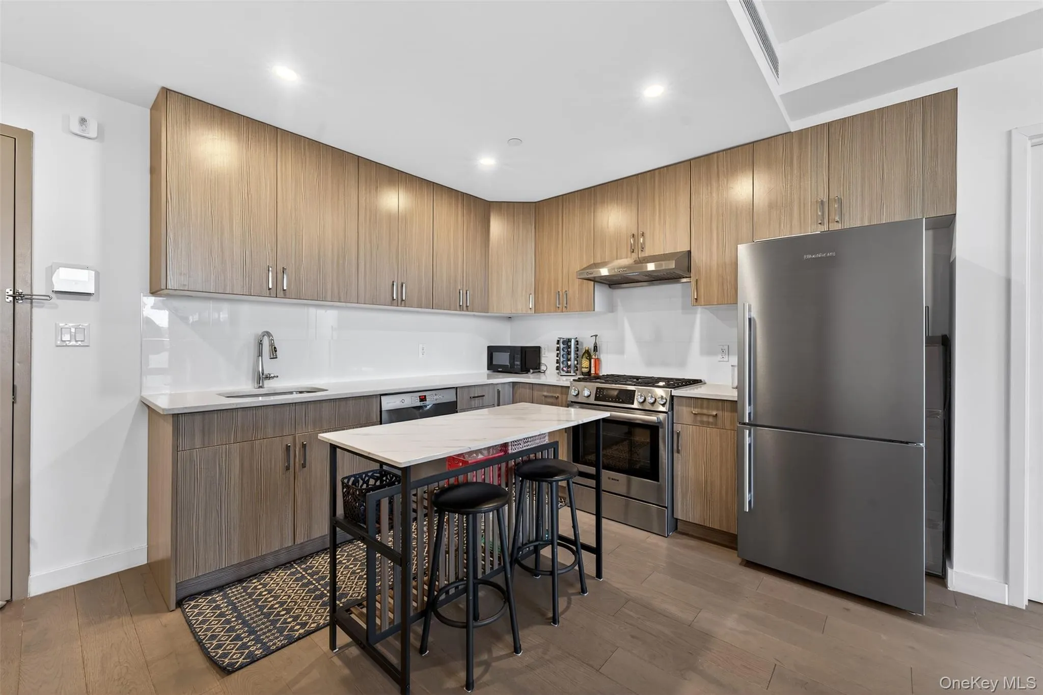 Kitchen featuring appliances with stainless steel finishes, light wood-type flooring, under cabinet range hood, light stone counters, and recessed lighting Kitchen featuring appliances with stainless steel finishes, light wood-type flooring, under cabinet range hood, light stone counters, and recessed lighting