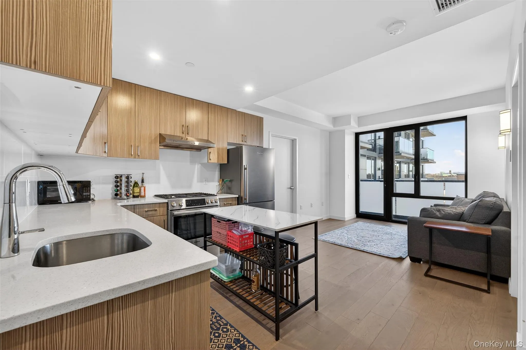 Kitchen featuring light stone counters, light wood-type flooring, appliances with stainless steel finishes, open floor plan, and under cabinet range hood Kitchen featuring light stone counters, light wood-type flooring, appliances with stainless steel finishes, open floor plan, and under cabinet range hood