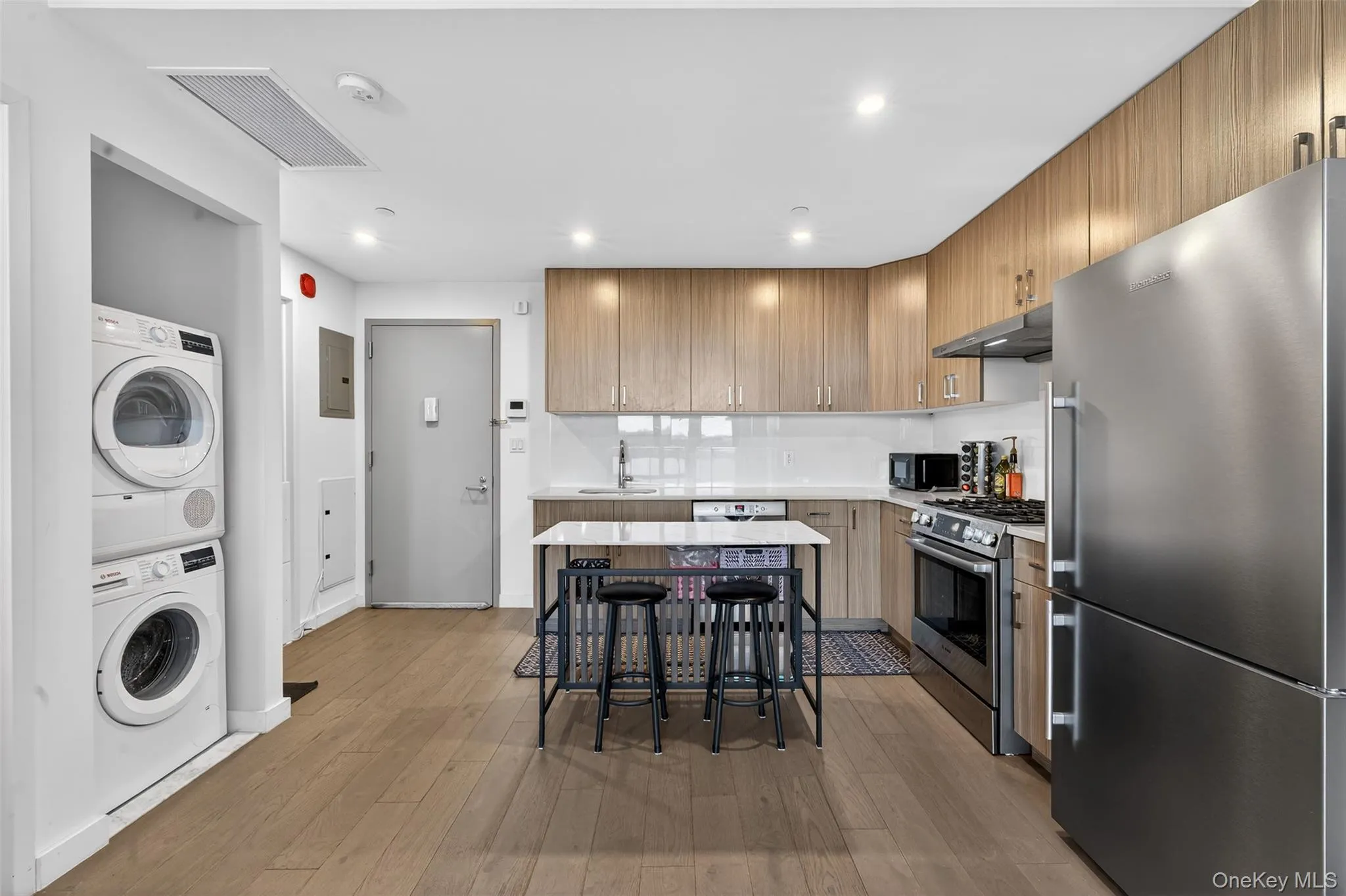Kitchen featuring stainless steel appliances, light wood finished floors, recessed lighting, electric panel, and stacked washer / drying machine Kitchen featuring stainless steel appliances, light wood finished floors, recessed lighting, electric panel, and stacked washer / drying machine