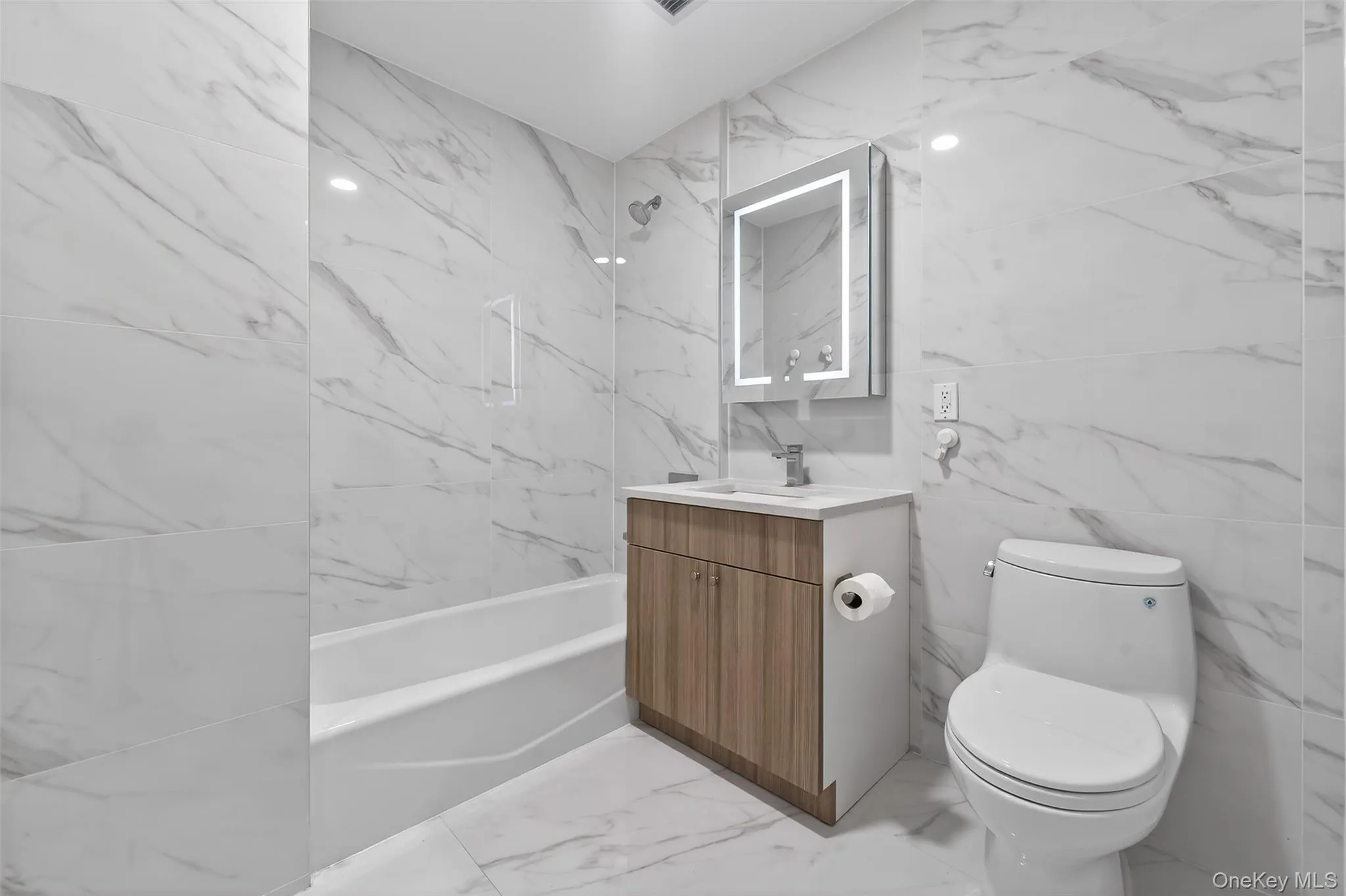 Full bathroom featuring light marble finish flooring, tile walls, a combined bath / shower with marble appearance, vanity, and stone wall Full bathroom featuring light marble finish flooring, tile walls, a combined bath / shower with marble appearance, vanity, and stone wall