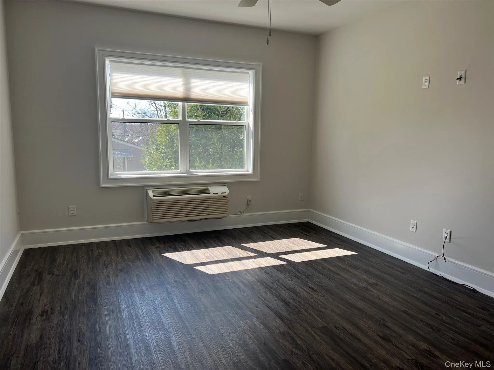 Empty room with a ceiling fan, dark wood-style floors, and a wall mounted air conditioner Empty room with a ceiling fan, dark wood-style floors, and a wall mounted air conditioner