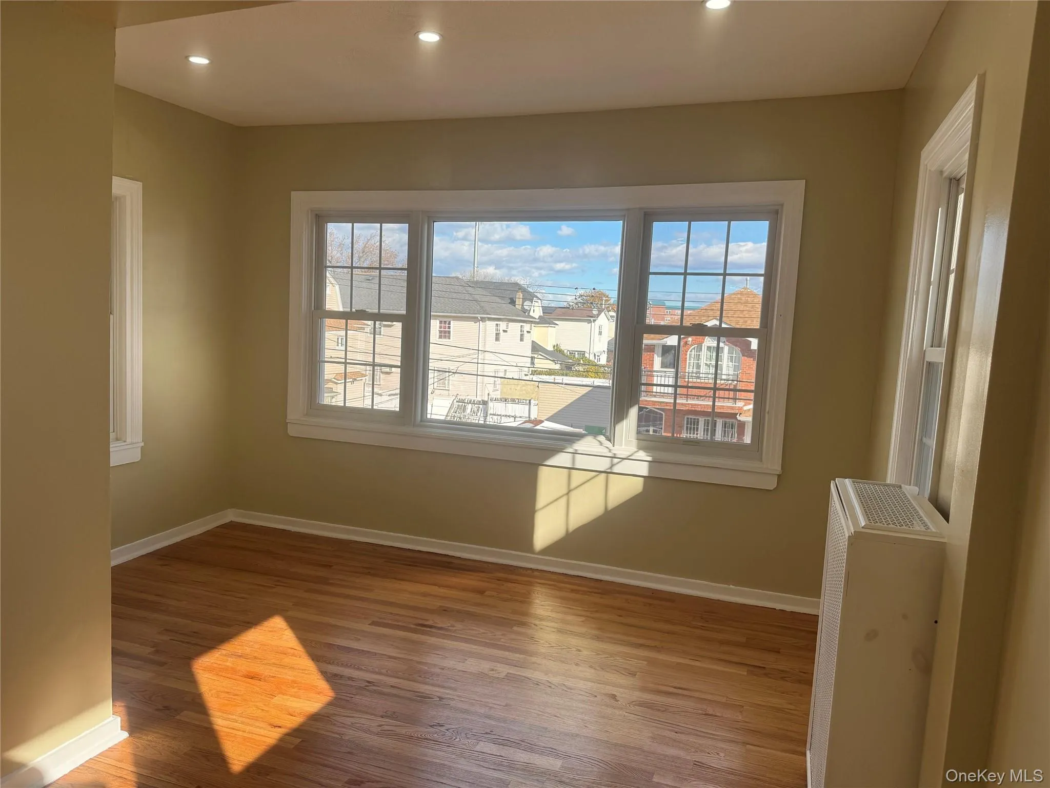Empty room with wood finished floors, recessed lighting, and radiator heating unit Empty room with wood finished floors, recessed lighting, and radiator heating unit