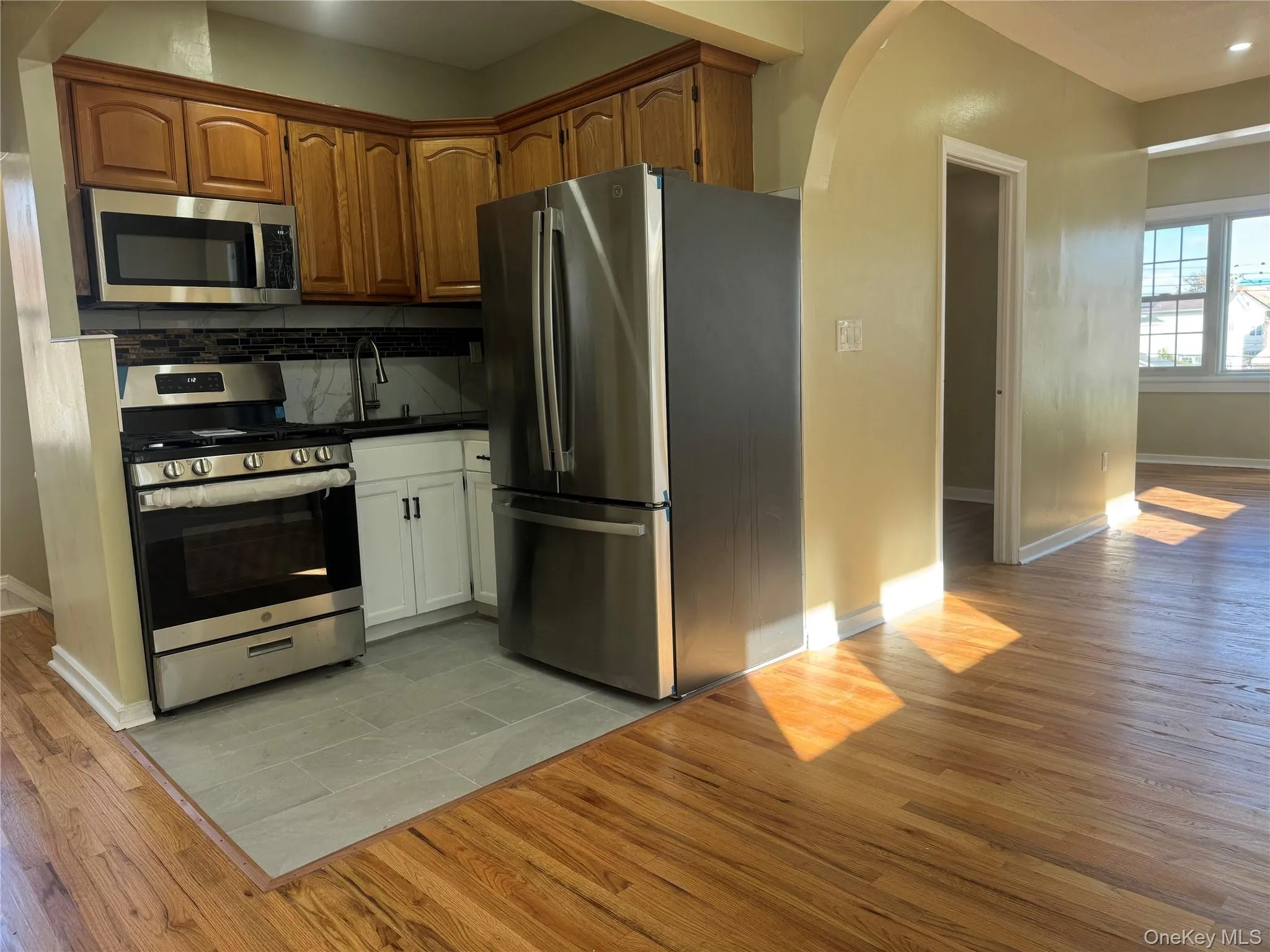 Kitchen featuring appliances with stainless steel finishes, arched walkways, light wood-style floors, and dark countertops Kitchen featuring appliances with stainless steel finishes, arched walkways, light wood-style floors, and dark countertops