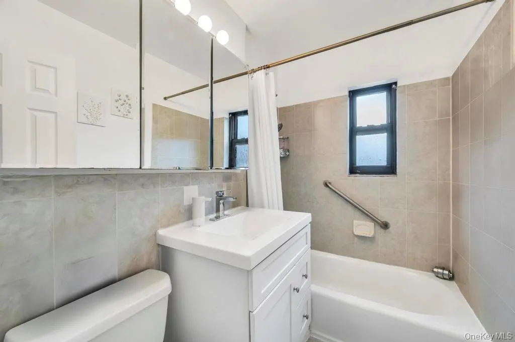 Bathroom featuring vanity, shower / bath combination with curtain, and tile walls Bathroom featuring vanity, shower / bath combination with curtain, and tile walls