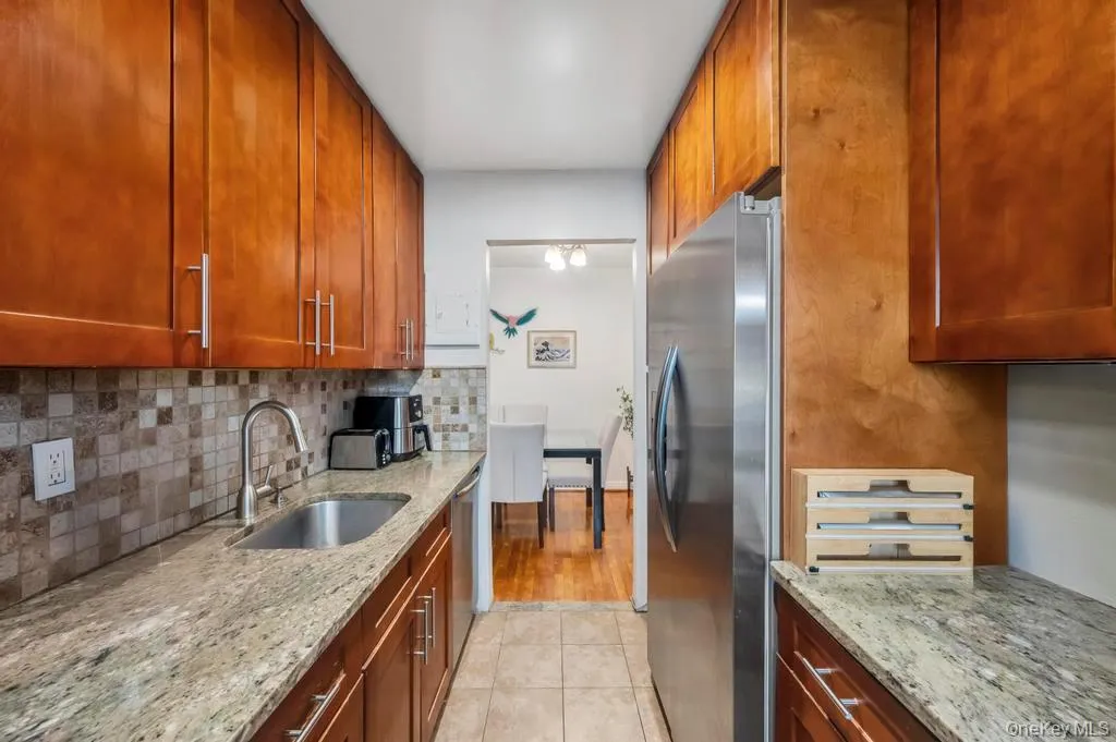 Kitchen featuring appliances with stainless steel finishes, light stone countertops, brown cabinets, and tasteful backsplash Kitchen featuring appliances with stainless steel finishes, light stone countertops, brown cabinets, and tasteful backsplash