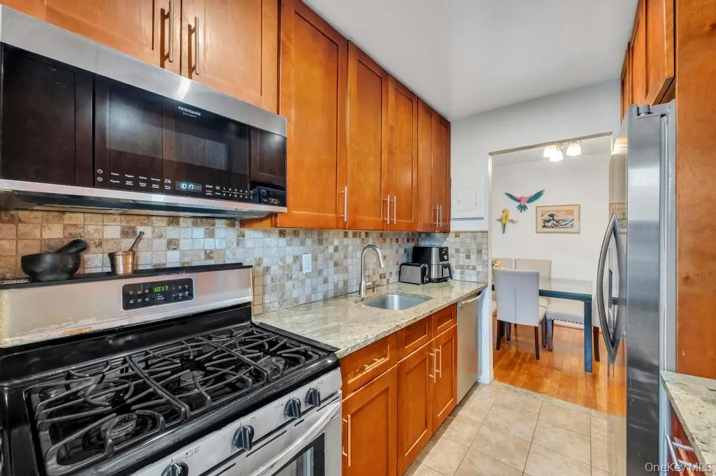 Kitchen featuring stainless steel appliances, light stone counters, brown cabinets, and decorative backsplash Kitchen featuring stainless steel appliances, light stone counters, brown cabinets, and decorative backsplash