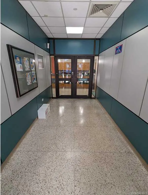 Hallway with a drop ceiling, dark speckled floor, and french doors Hallway with a drop ceiling, dark speckled floor, and french doors