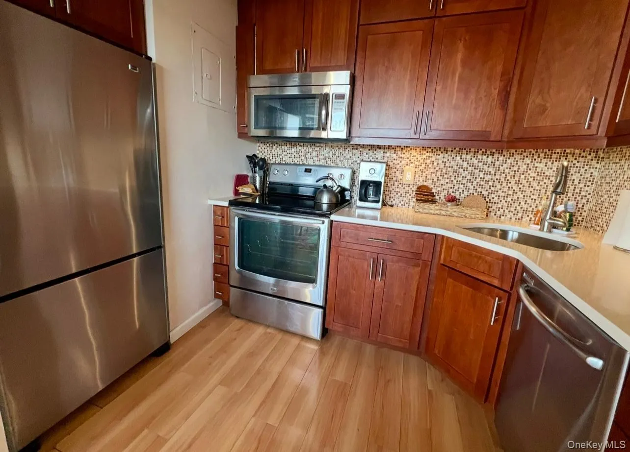 Kitchen with stainless steel appliances, tasteful backsplash, brown cabinets, light wood finished floors, and light stone countertops Kitchen with stainless steel appliances, tasteful backsplash, brown cabinets, light wood finished floors, and light stone countertops