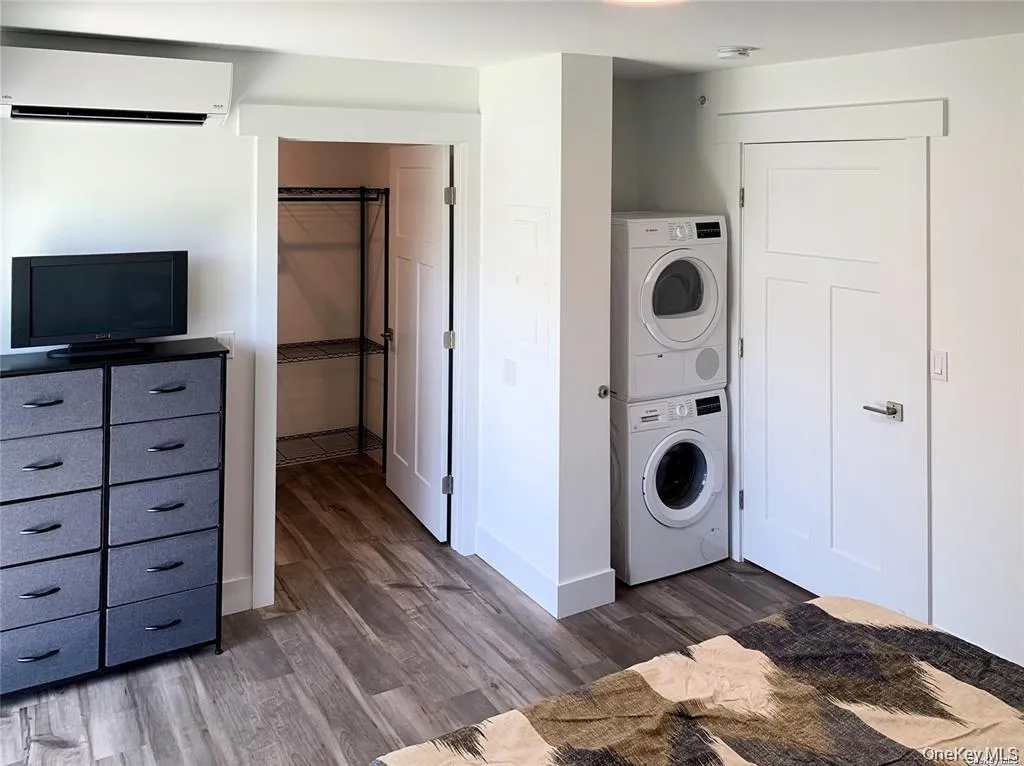 Washroom featuring a wall mounted AC, dark wood-style flooring, and stacked washer / drying machine Washroom featuring a wall mounted AC, dark wood-style flooring, and stacked washer / drying machine