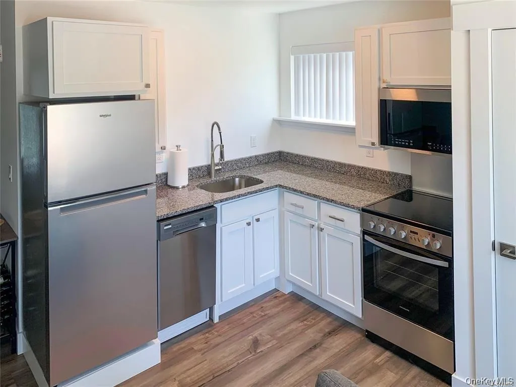 Kitchen featuring appliances with stainless steel finishes, white cabinetry, dark stone countertops, and light wood-style floors Kitchen featuring appliances with stainless steel finishes, white cabinetry, dark stone countertops, and light wood-style floors