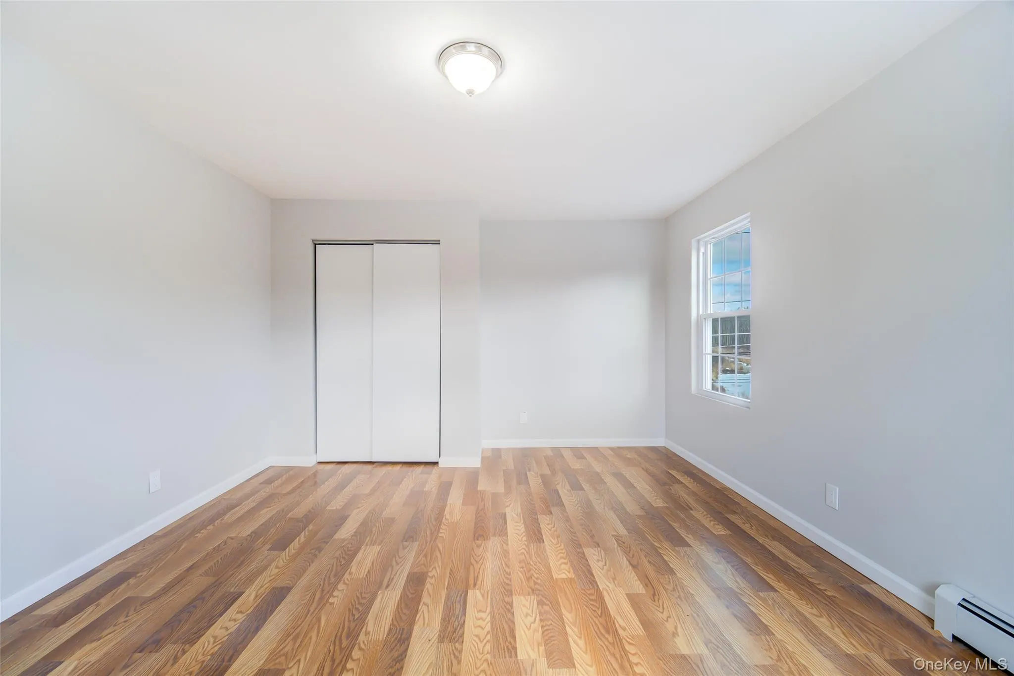 Bedroom with light wood finished floors, a closet, and a baseboard heating unit Bedroom with light wood finished floors, a closet, and a baseboard heating unit