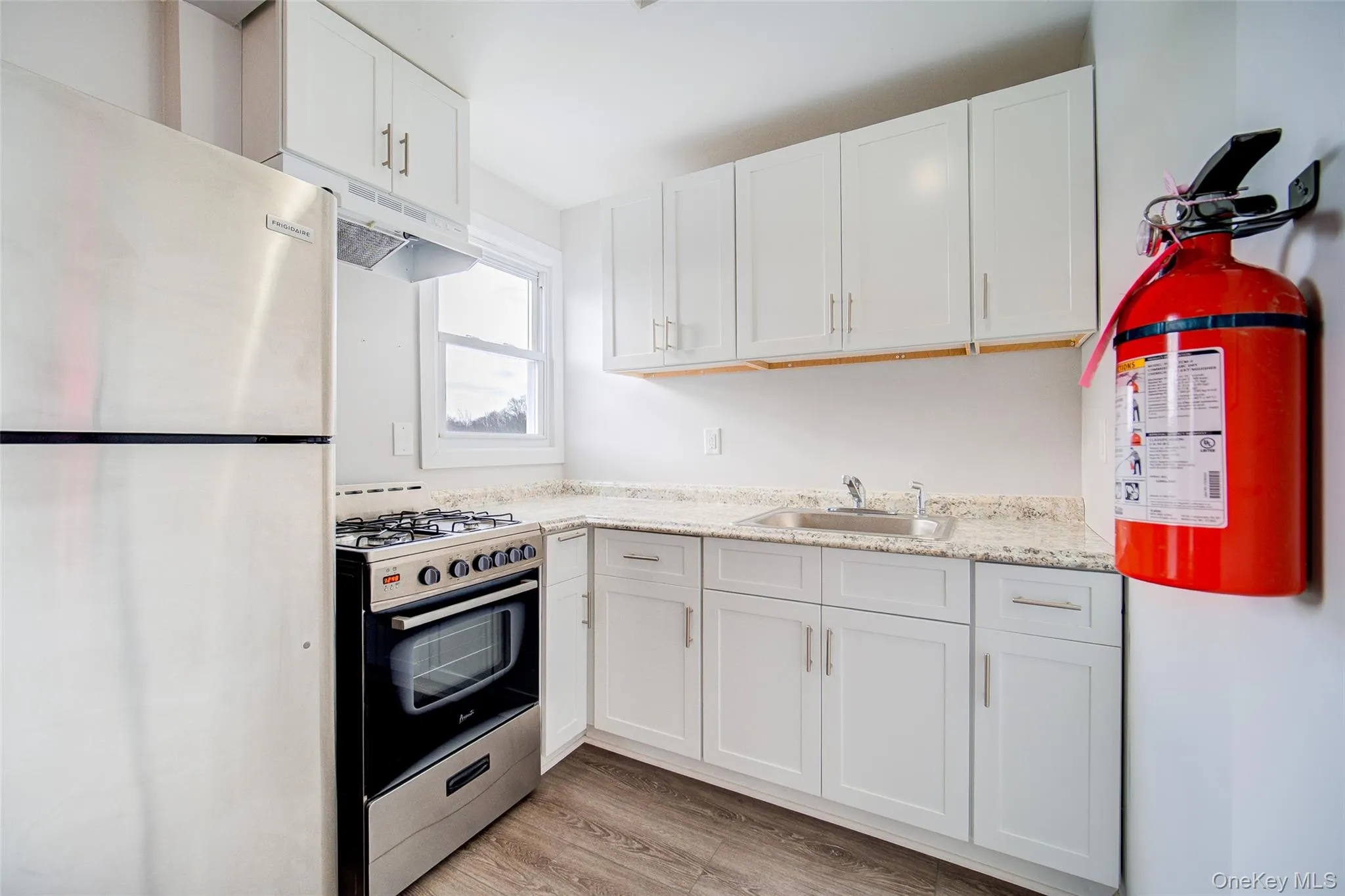 Kitchen with stainless steel appliances, white cabinets, light wood finished floors, light stone countertops, and under cabinet range hood Kitchen with stainless steel appliances, white cabinets, light wood finished floors, light stone countertops, and under cabinet range hood