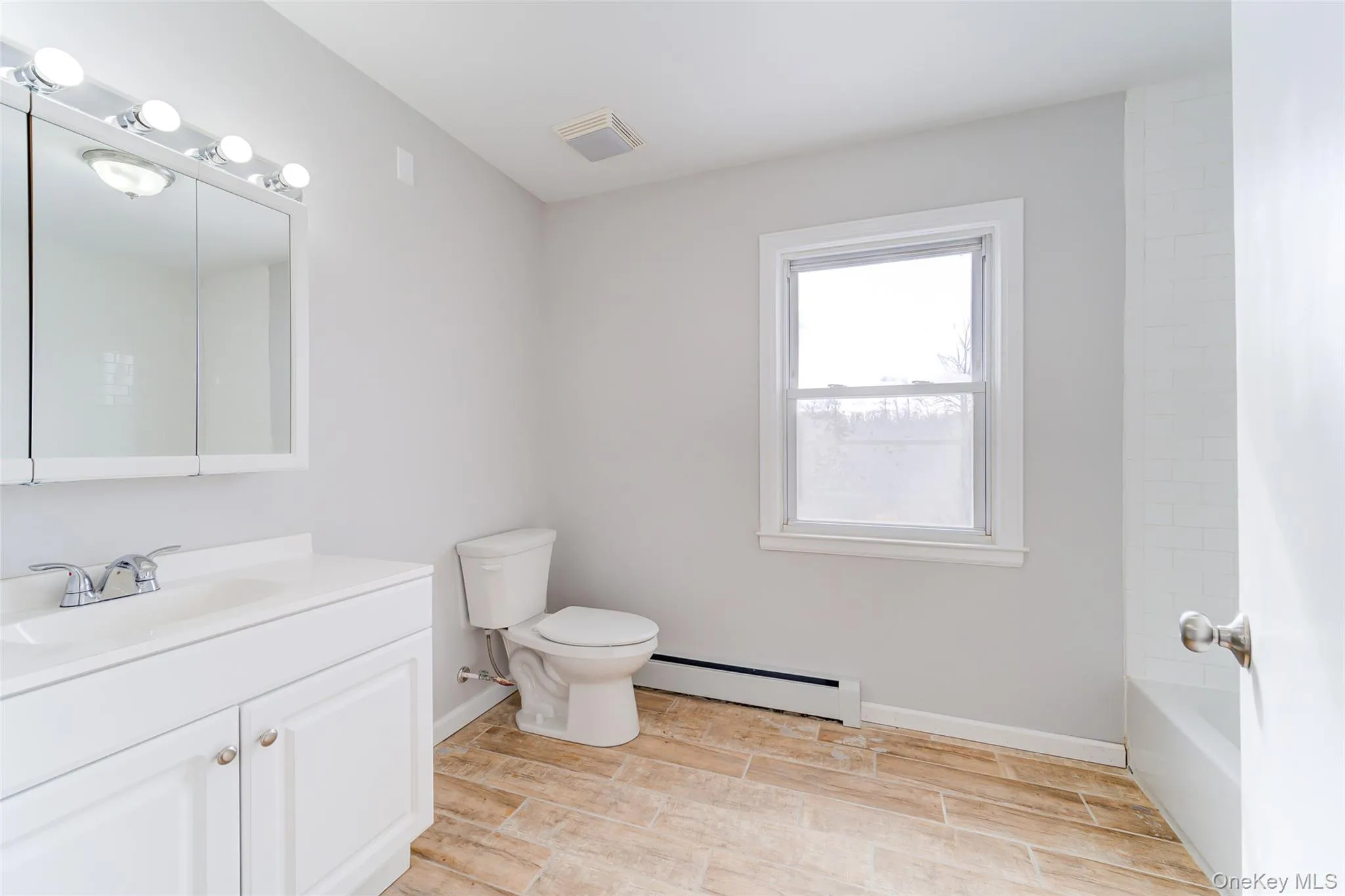 Full bathroom featuring vanity, baseboard heating, wood finish floors, and shower / bath combination Full bathroom featuring vanity, baseboard heating, wood finish floors, and shower / bath combination