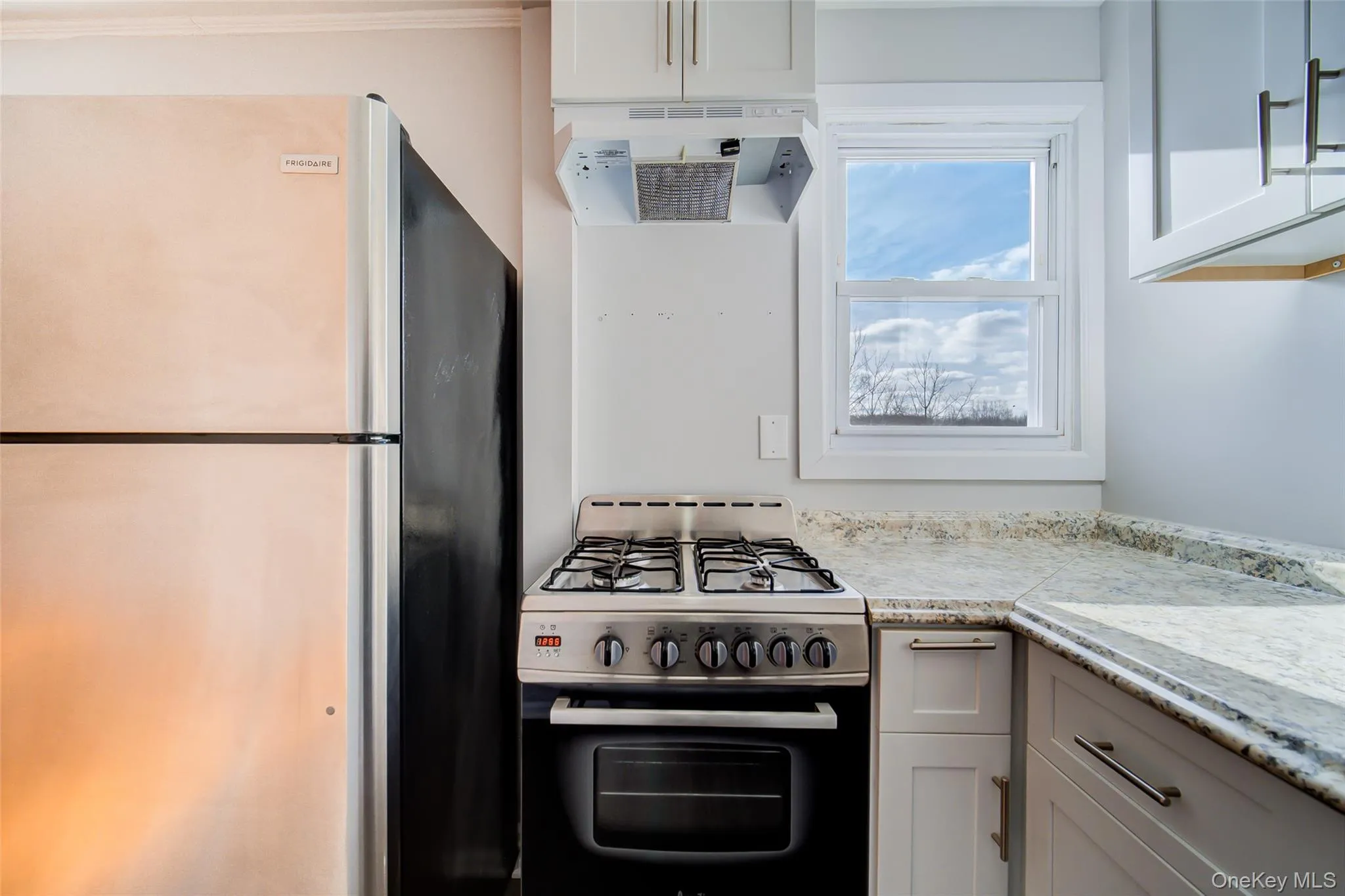 Kitchen with freestanding refrigerator, gas range, fan, white cabinets, and gray cabinetry Kitchen with freestanding refrigerator, gas range, fan, white cabinets, and gray cabinetry