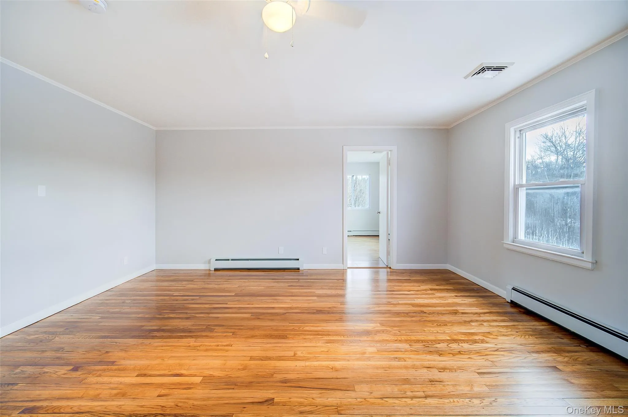 Living room with view into bedroom featuring a baseboard heating unit, light wood-style flooring, ornamental molding, a ceiling fan, and a baseboard radiator Living room with view into bedroom featuring a baseboard heating unit, light wood-style flooring, ornamental molding, a ceiling fan, and a baseboard radiator