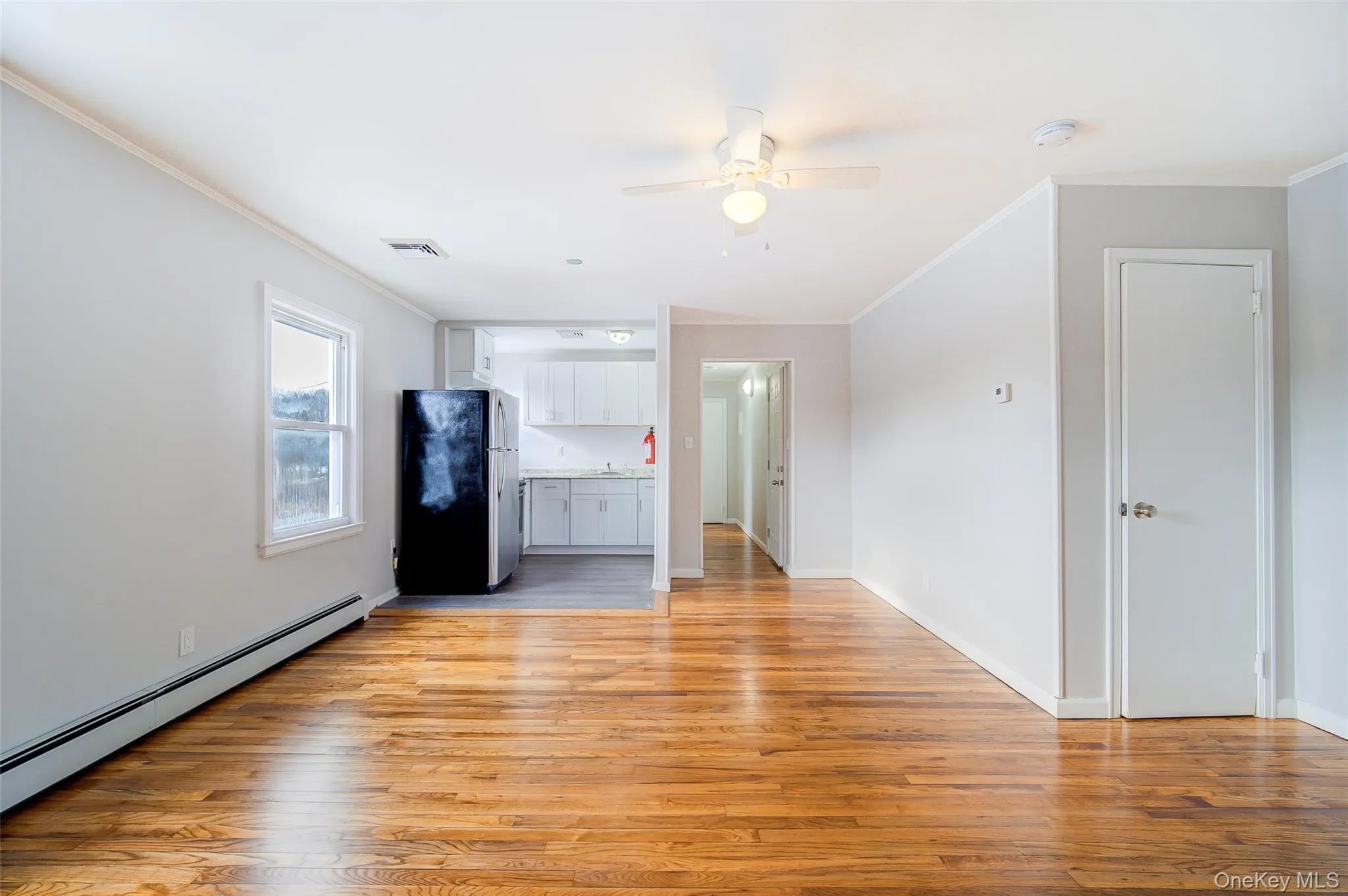 View from living room looking into kitchen with crown molding, baseboard heating, light wood-type flooring, and a ceiling fan View from living room looking into kitchen with crown molding, baseboard heating, light wood-type flooring, and a ceiling fan