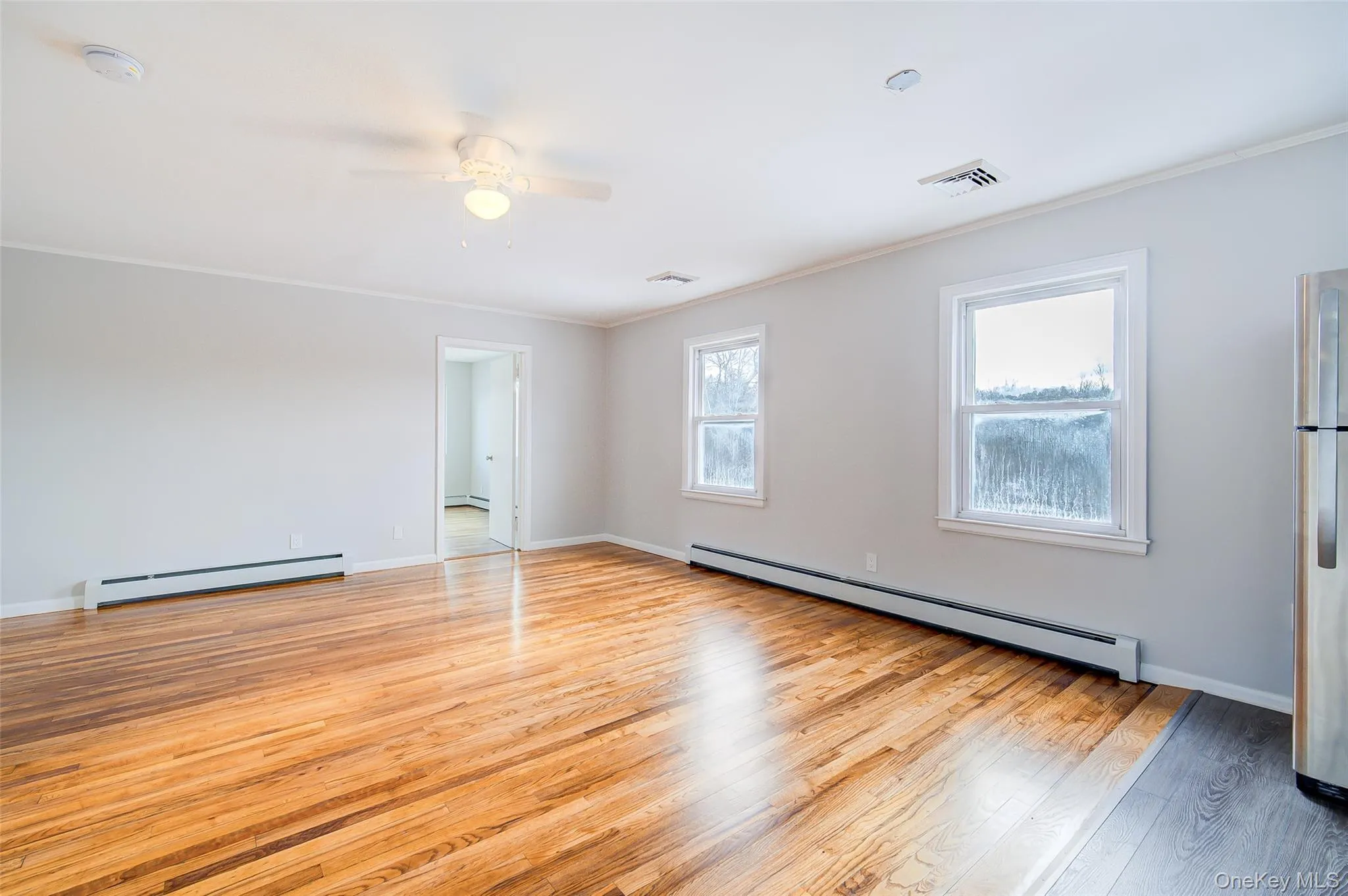 View of living room area with baseboards, light wood-type flooring, baseboard heating, ornamental molding, and ceiling fan View of living room area with baseboards, light wood-type flooring, baseboard heating, ornamental molding, and ceiling fan