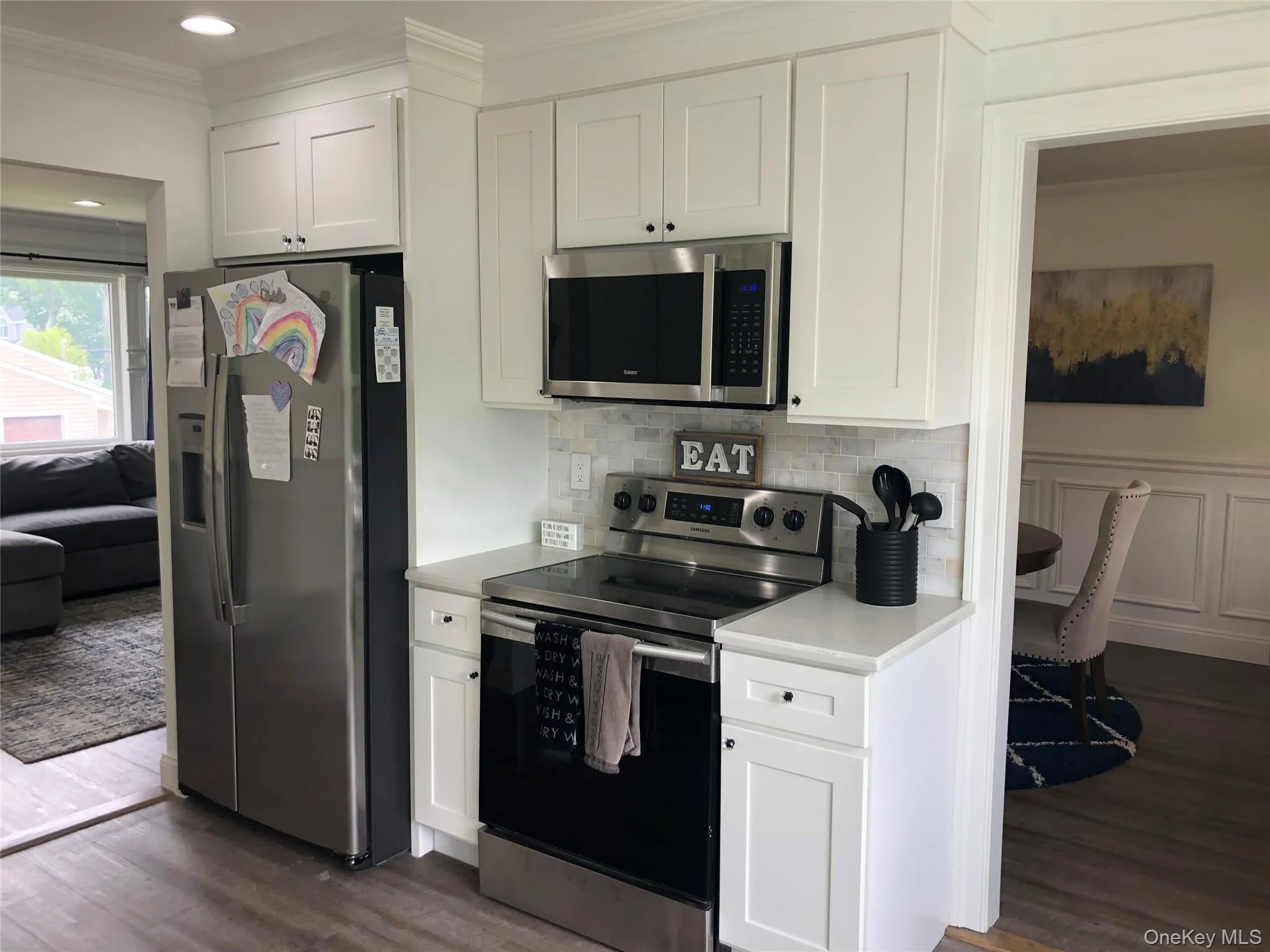 Kitchen with appliances with stainless steel finishes, light countertops, white cabinetry, dark wood-style flooring, and crown molding Kitchen with appliances with stainless steel finishes, light countertops, white cabinetry, dark wood-style flooring, and crown molding